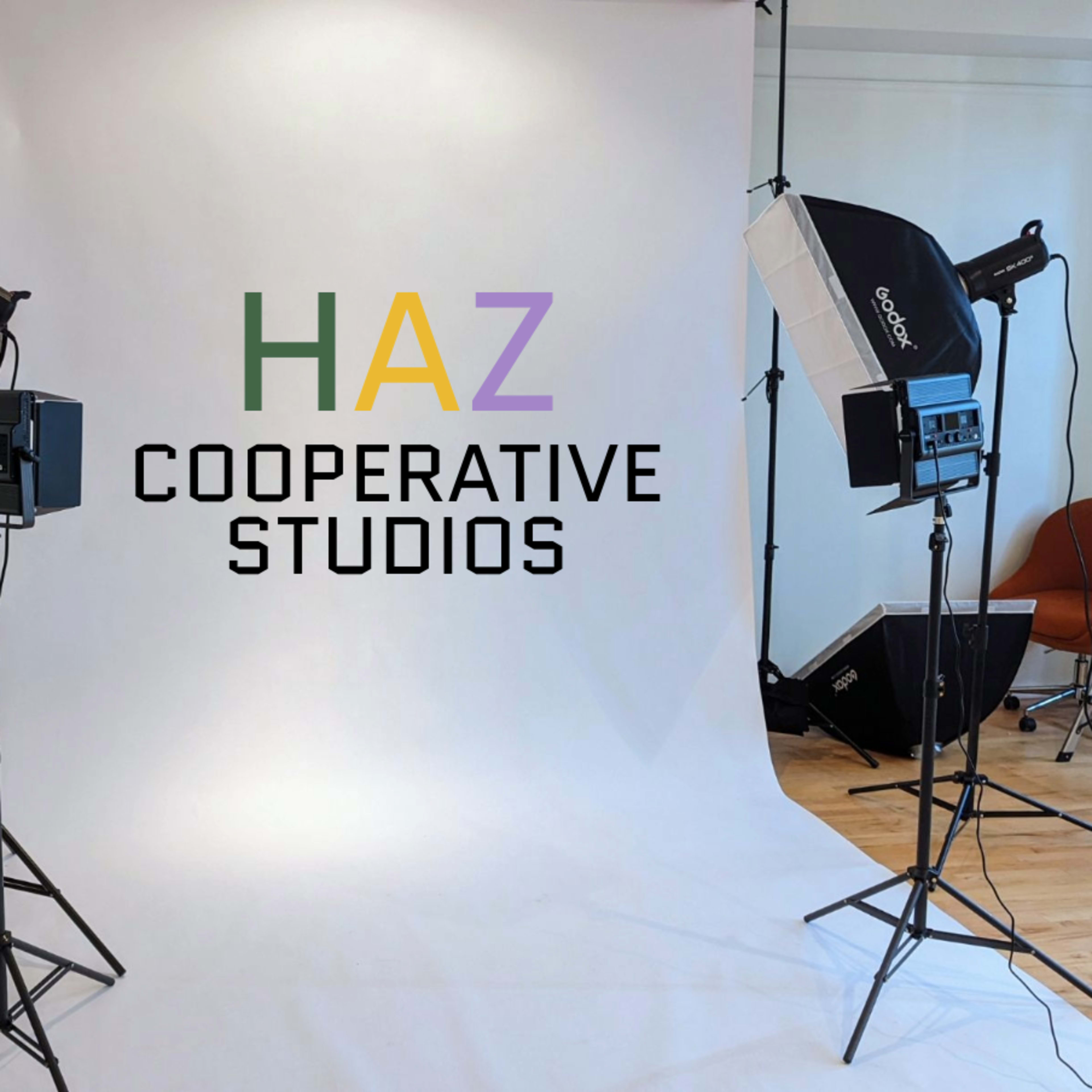 A photography studio setup with lights, softboxes, and a large white backdrop, featuring the text "HAZ COOPERATIVE STUDIOS" in bold letters.