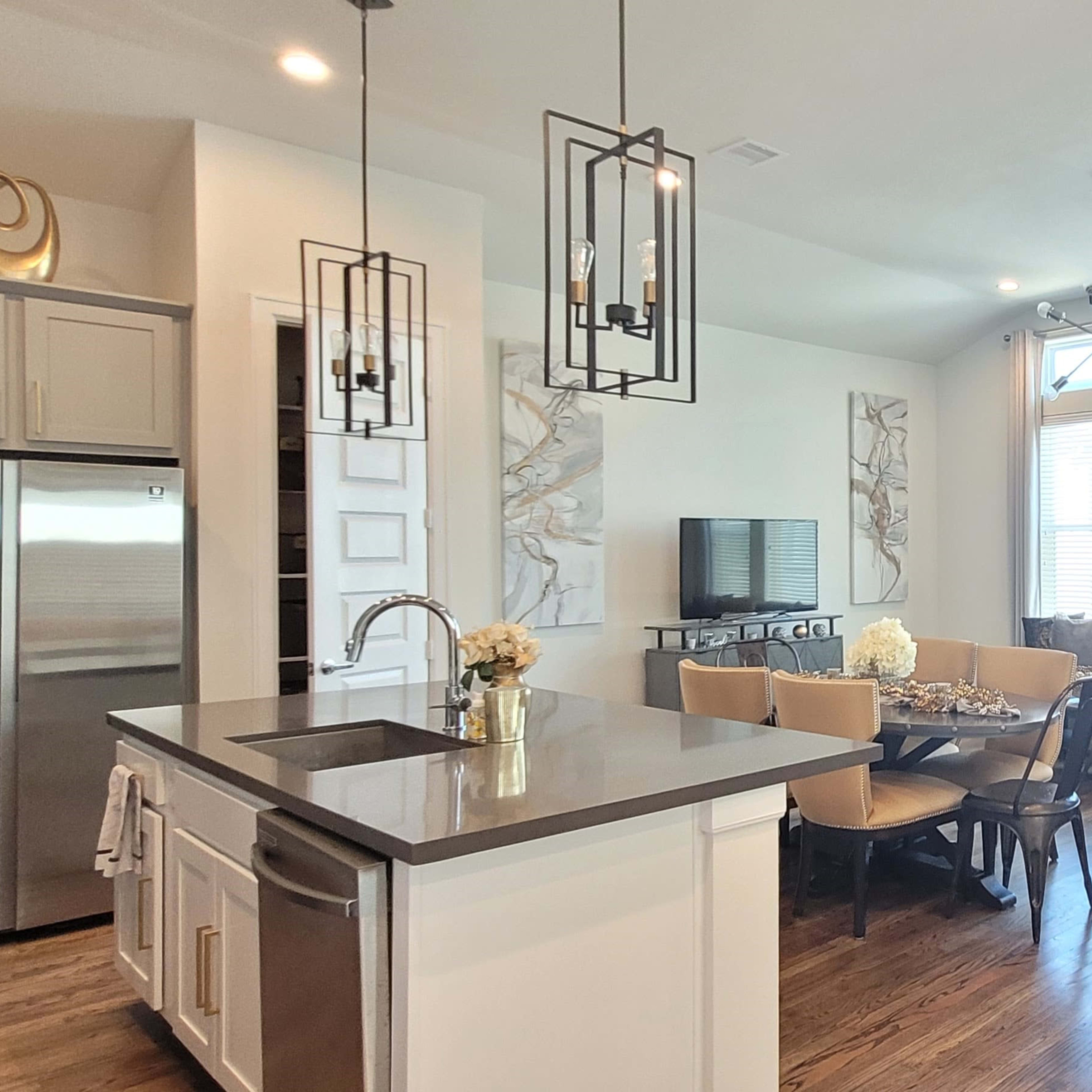 A modern kitchen and living room area with a central island, stainless steel appliances, and a sectional sofa near large windows.