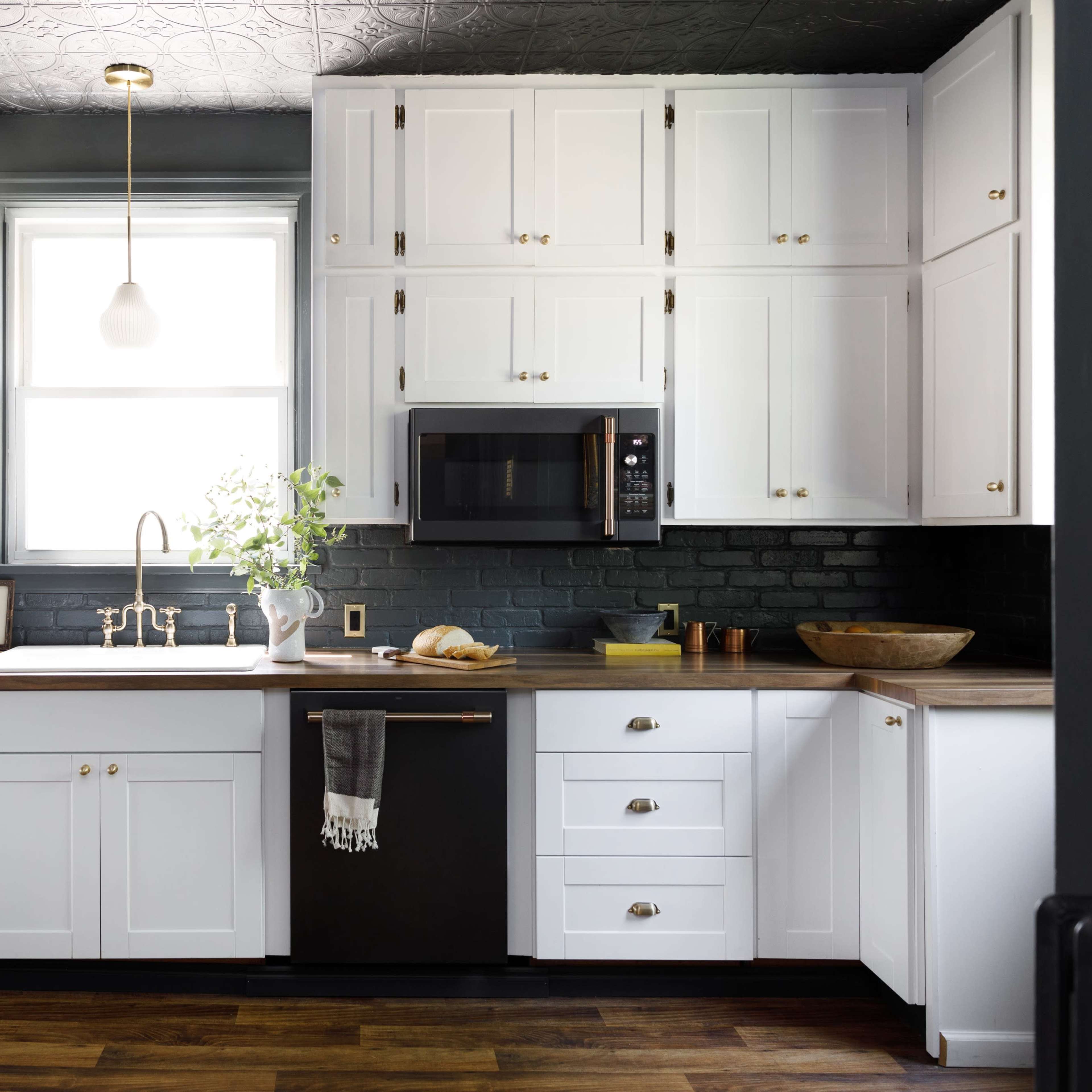 The kitchen features white cabinets, a dark countertop, a stainless steel microwave, and a farmhouse sink with a window above it.