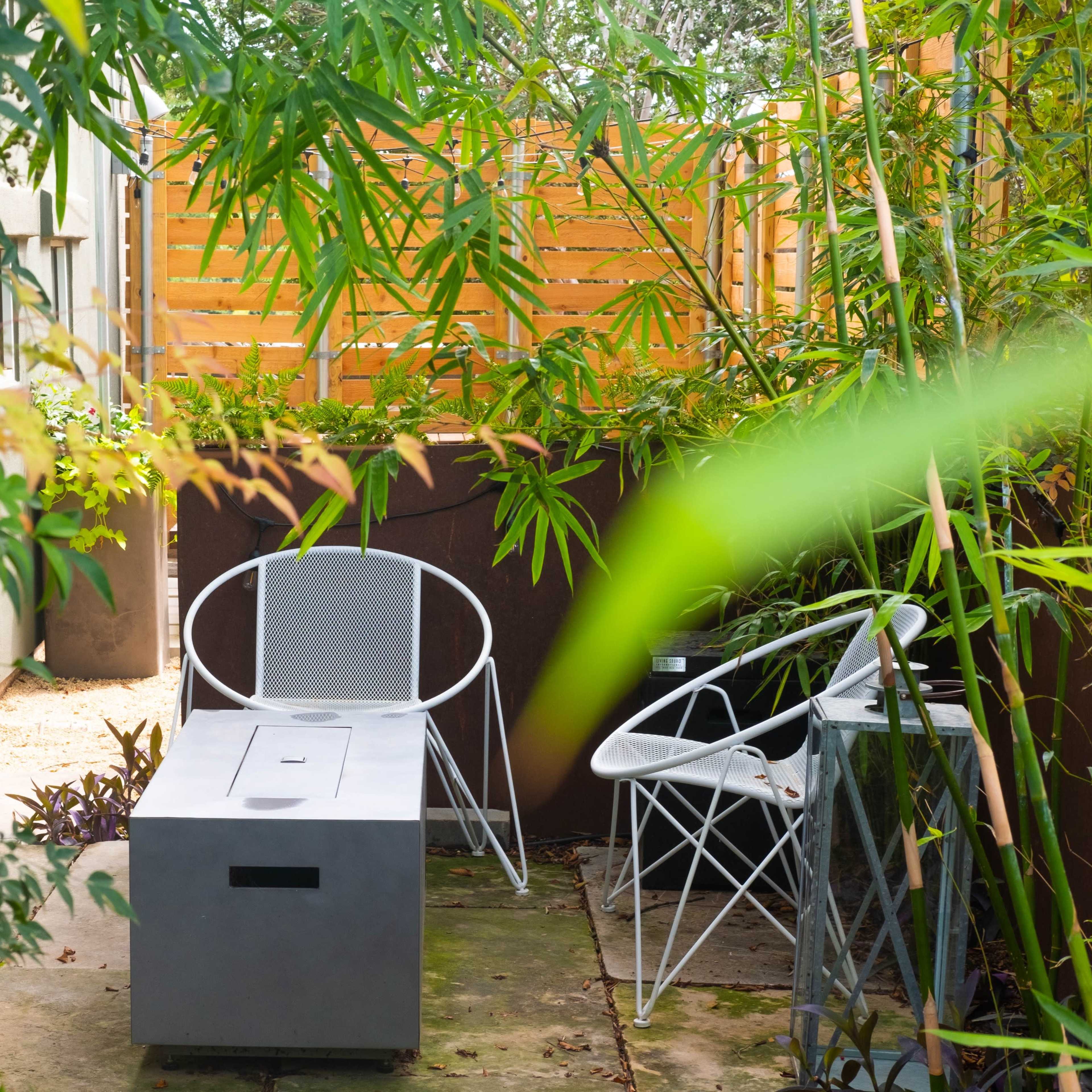 A cozy outdoor seating area surrounded by greenery, featuring two chairs and a rectangular table on a stone patio.