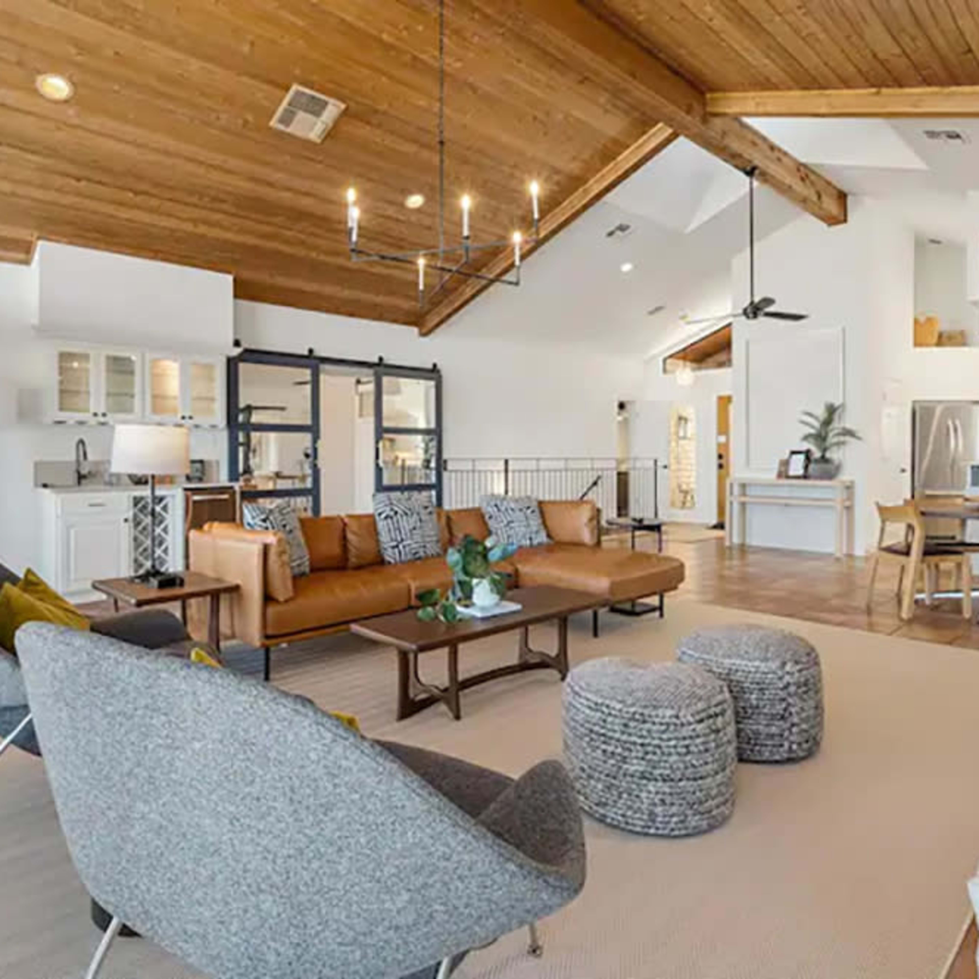 A spacious, modern living room with vaulted wood ceilings, a sofa, and a dining area connected to a kitchen.