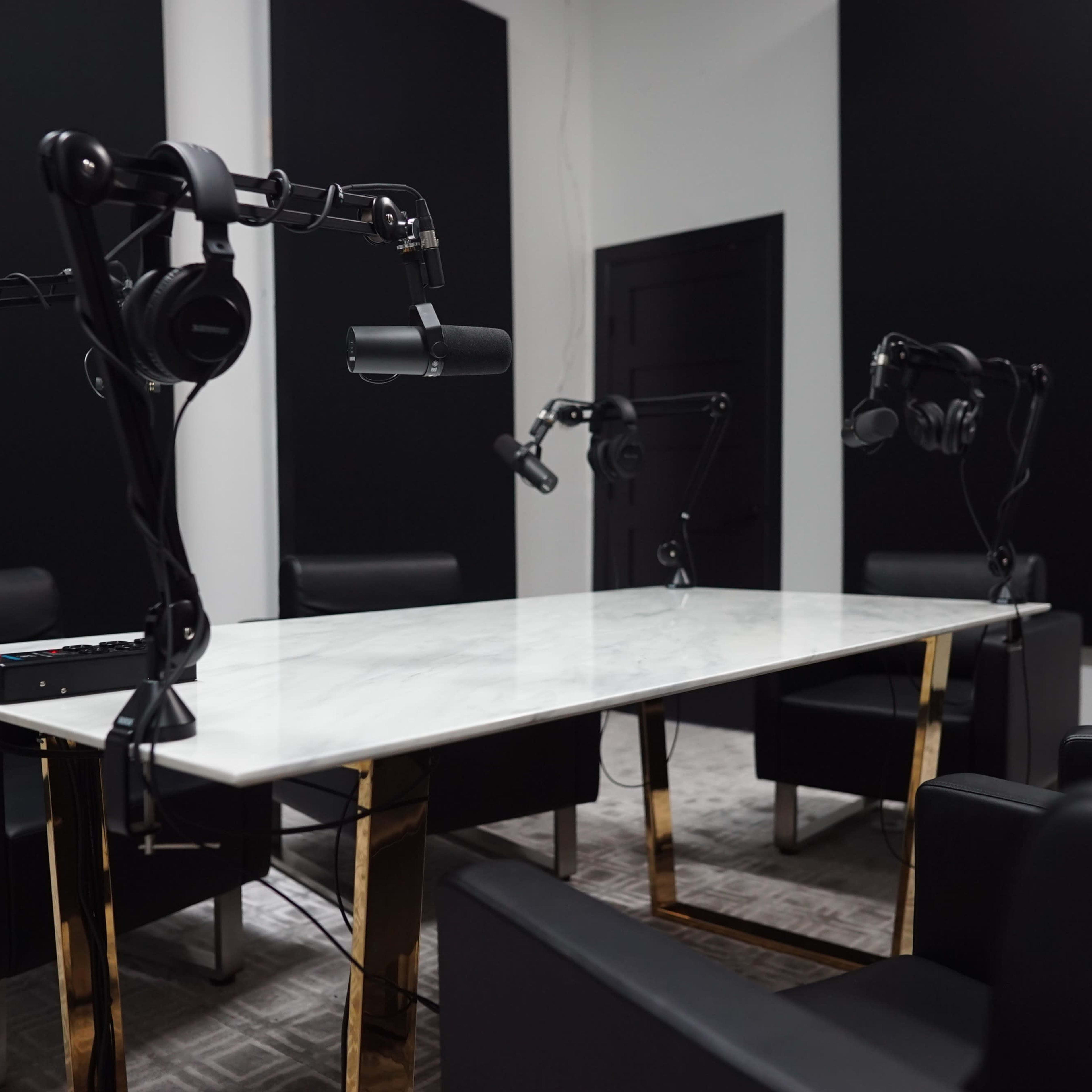 A podcast studio featuring a marble table surrounded by black chairs, with microphone stands and headphones positioned for recording.