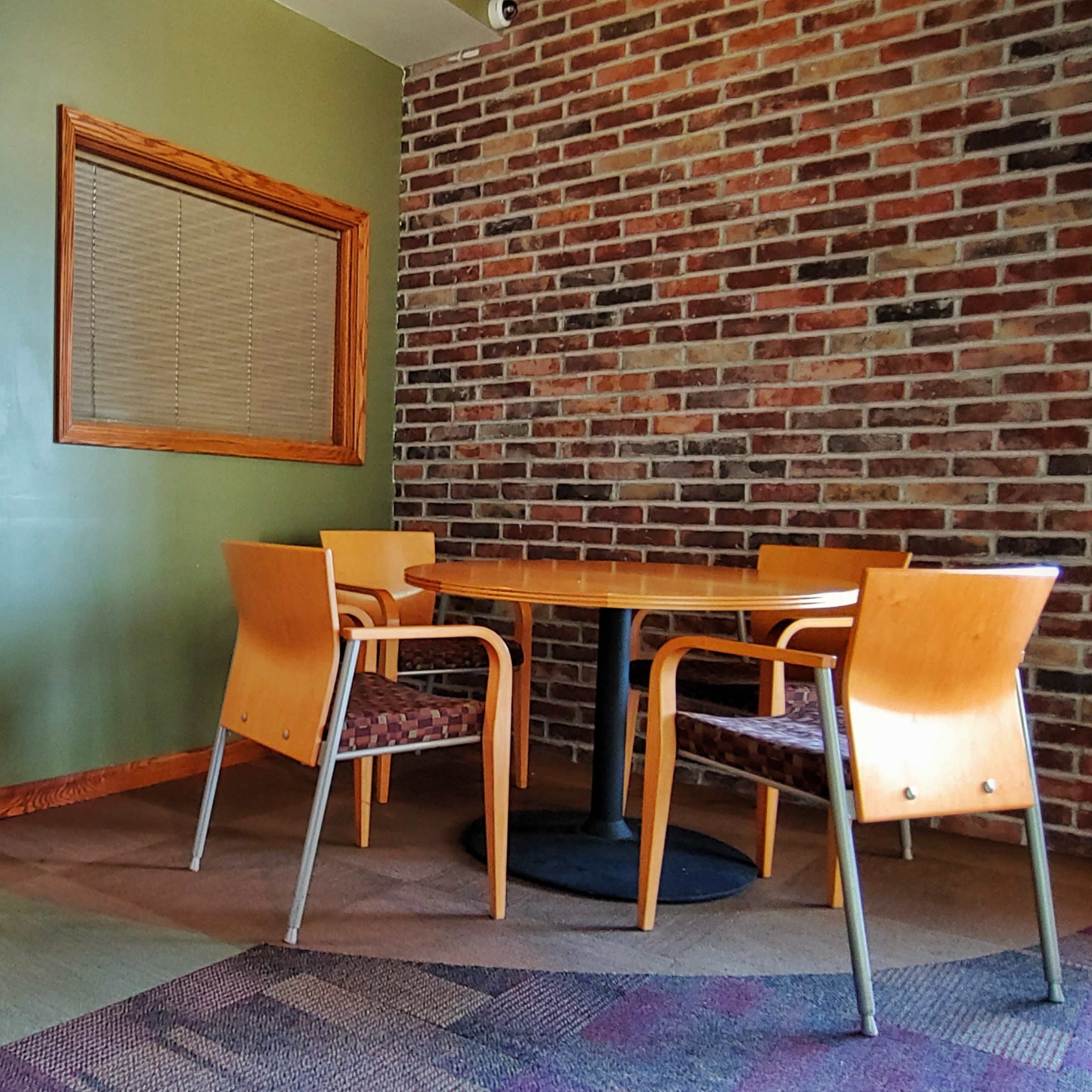 A corner of a room featuring a wooden table with two chairs, a brick wall, and an adjacent door.