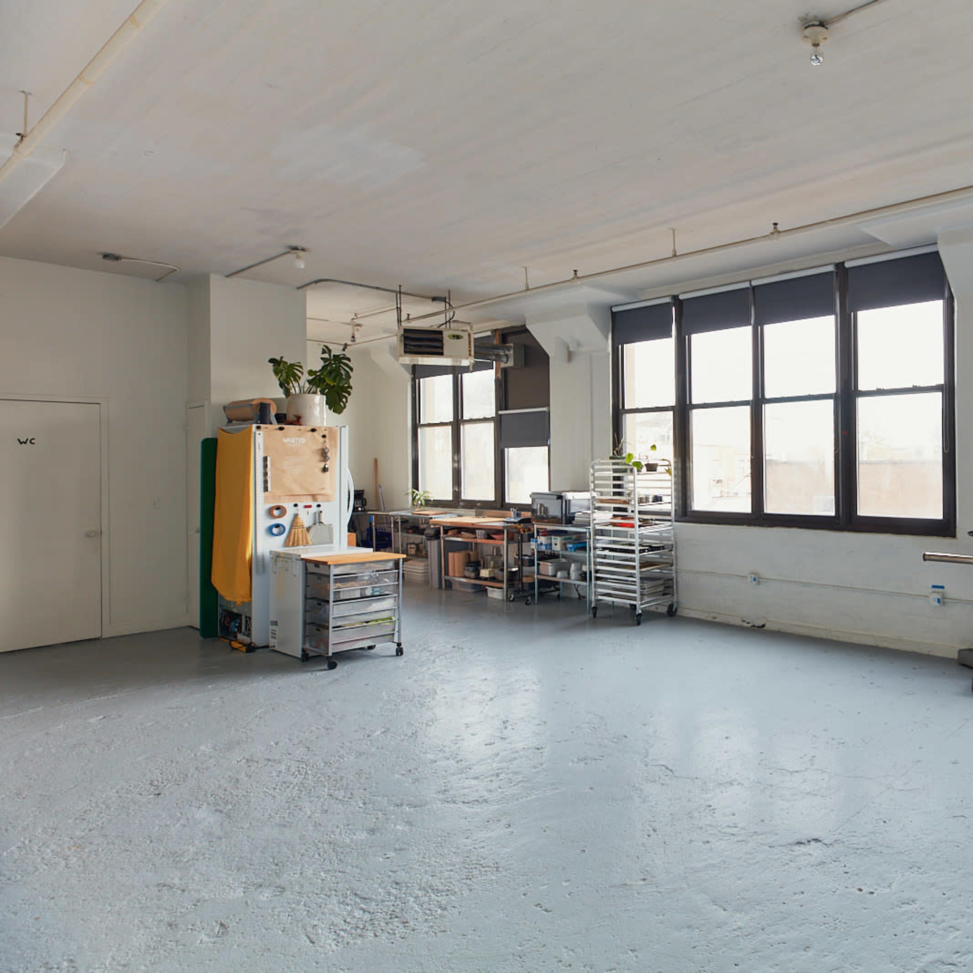 An open studio space with large windows, a wooden table, and various storage units against the walls.