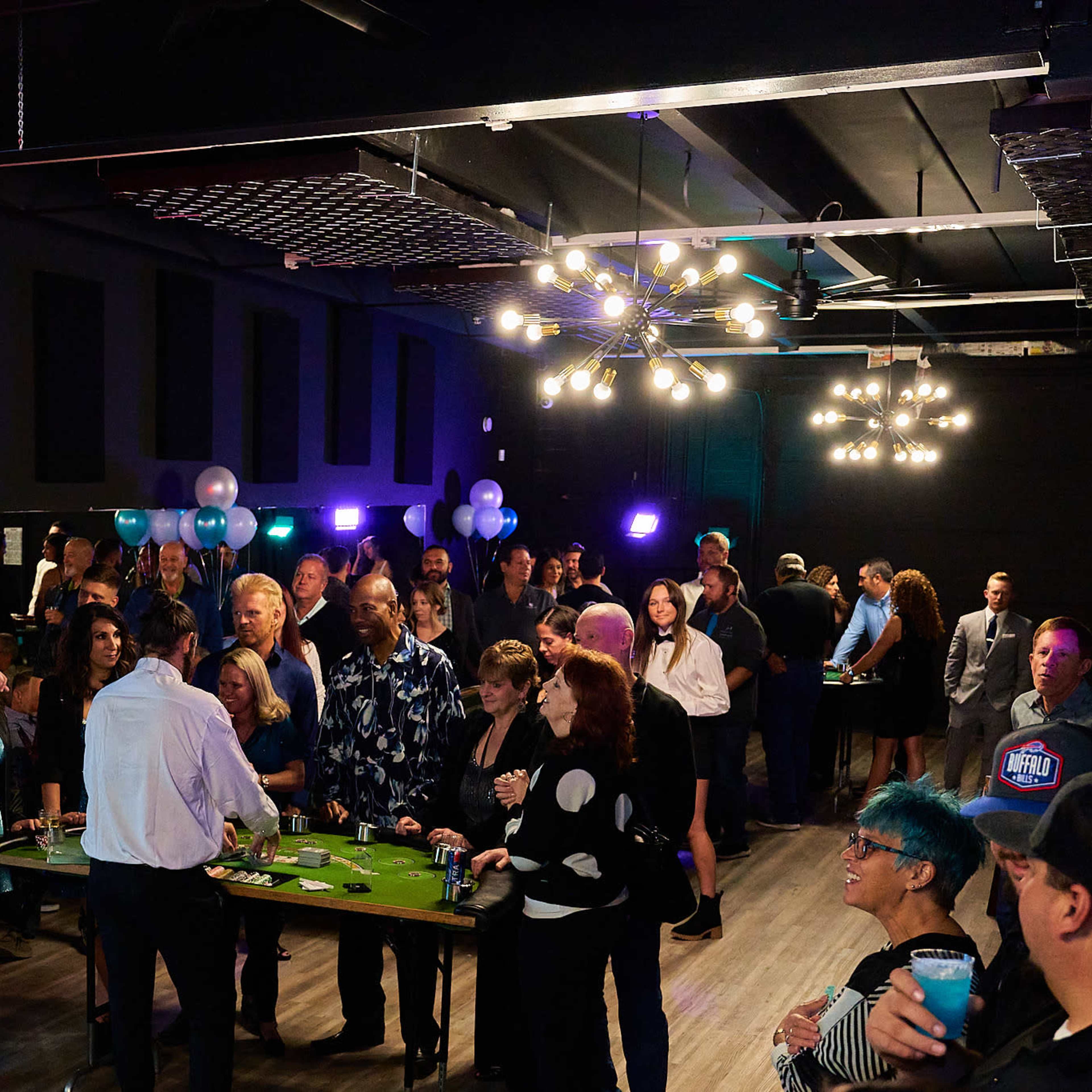 A large group of people gathers in a well-lit venue, participating in a social event with tables set up for gaming activities.