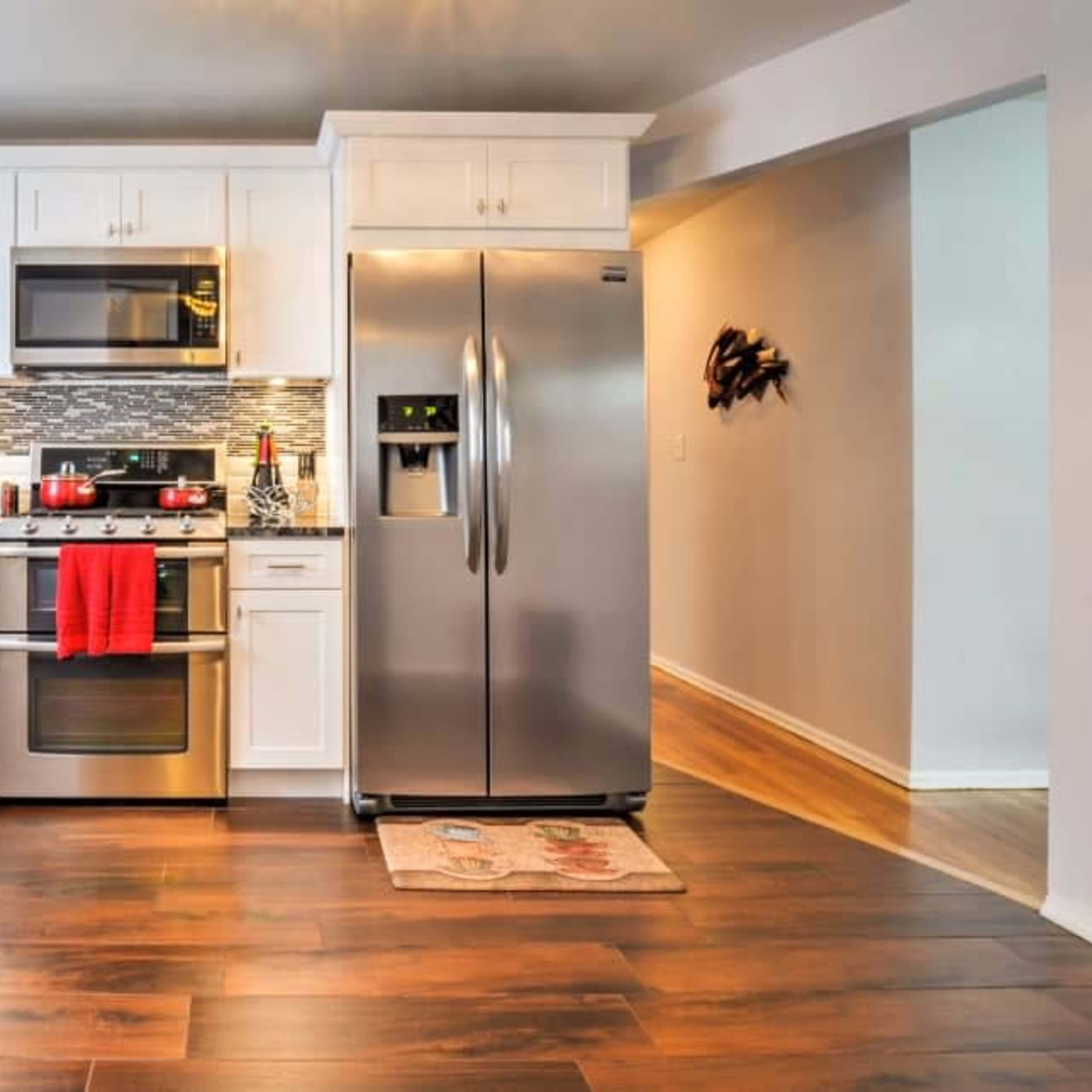 A modern kitchen with stainless steel appliances, white cabinets, and wooden flooring.