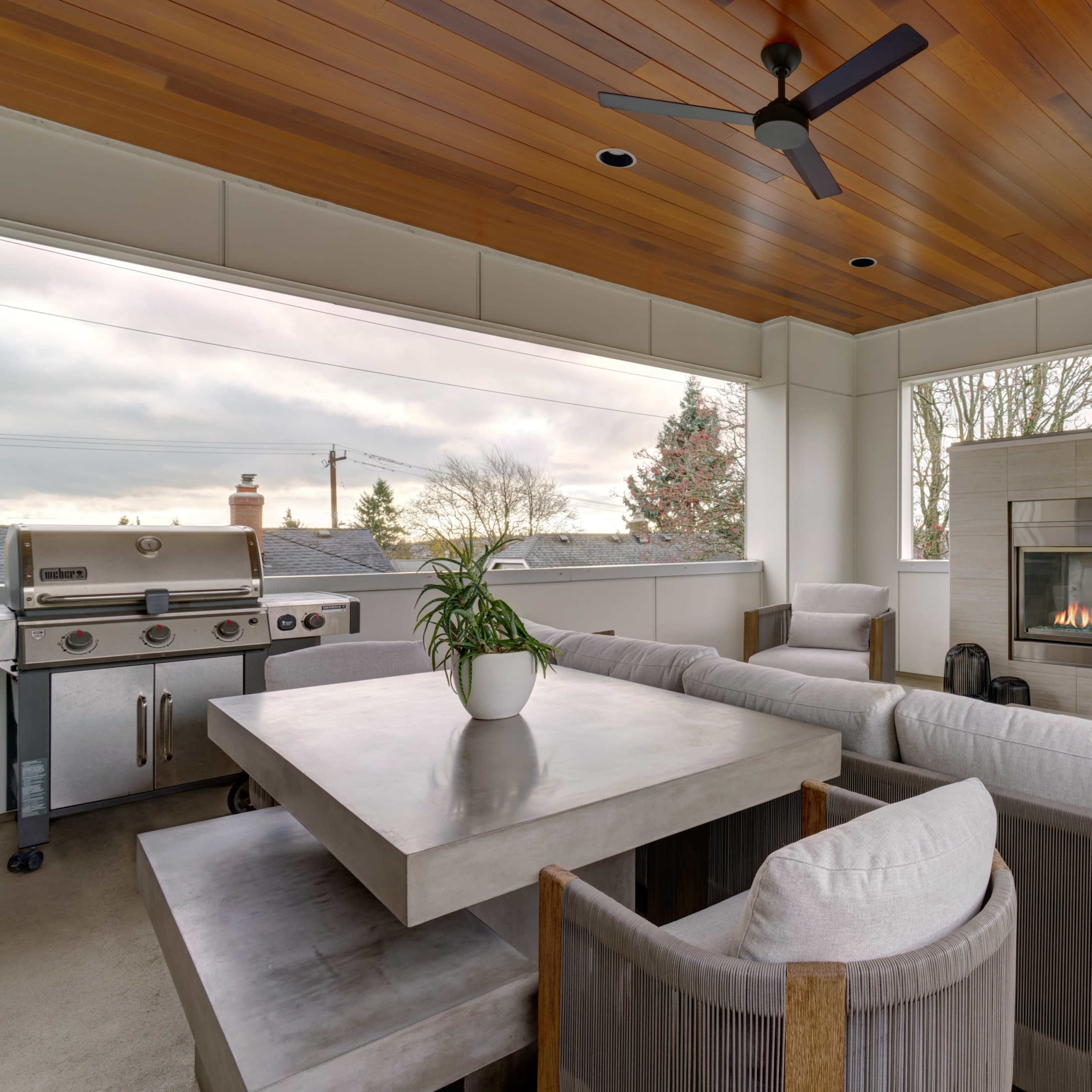 A modern outdoor patio with a built-in fireplace, a dining table, cushioned seating, and a grill.