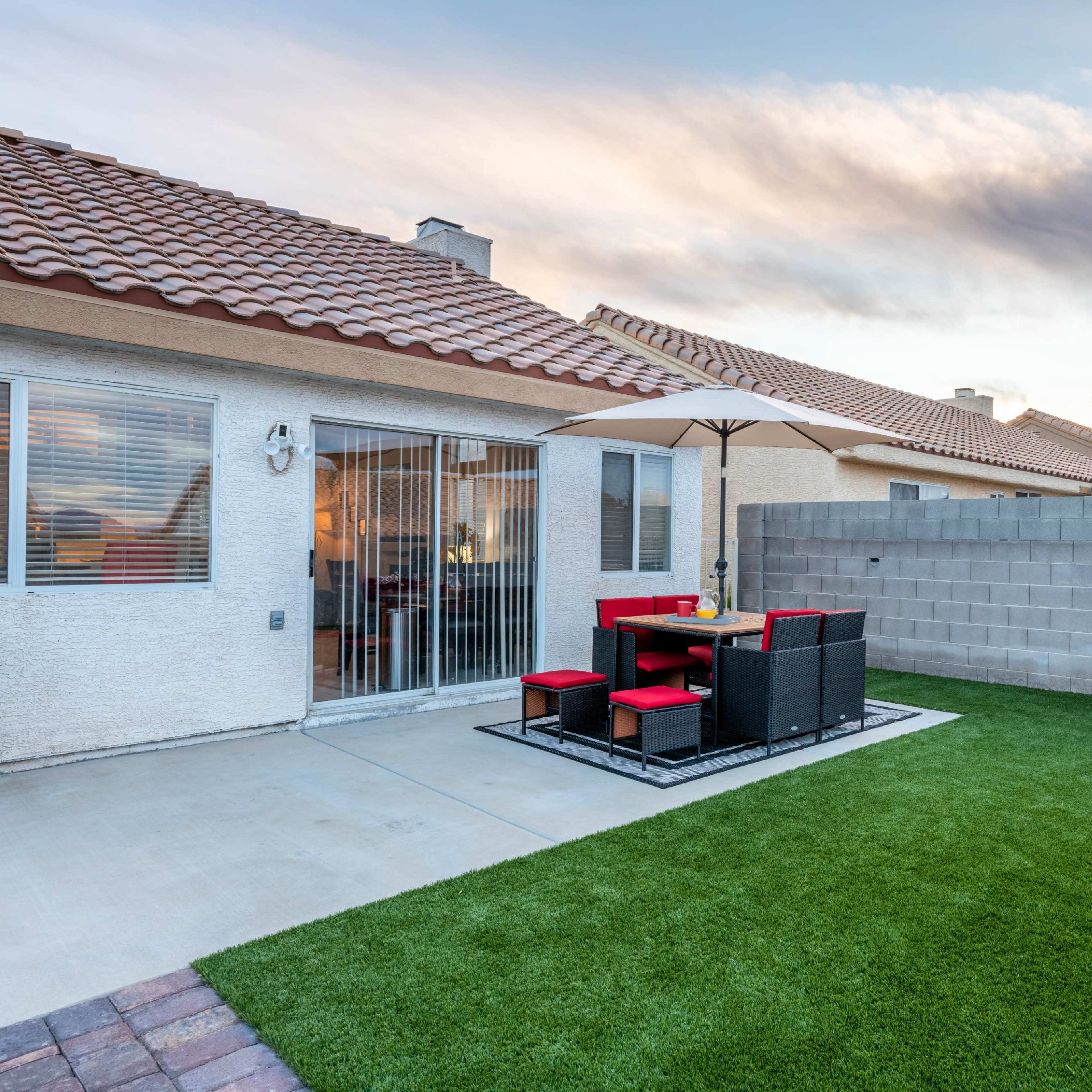 A backyard with artificial turf, a patio area with a table and chairs, and a sliding glass door leading into a house.