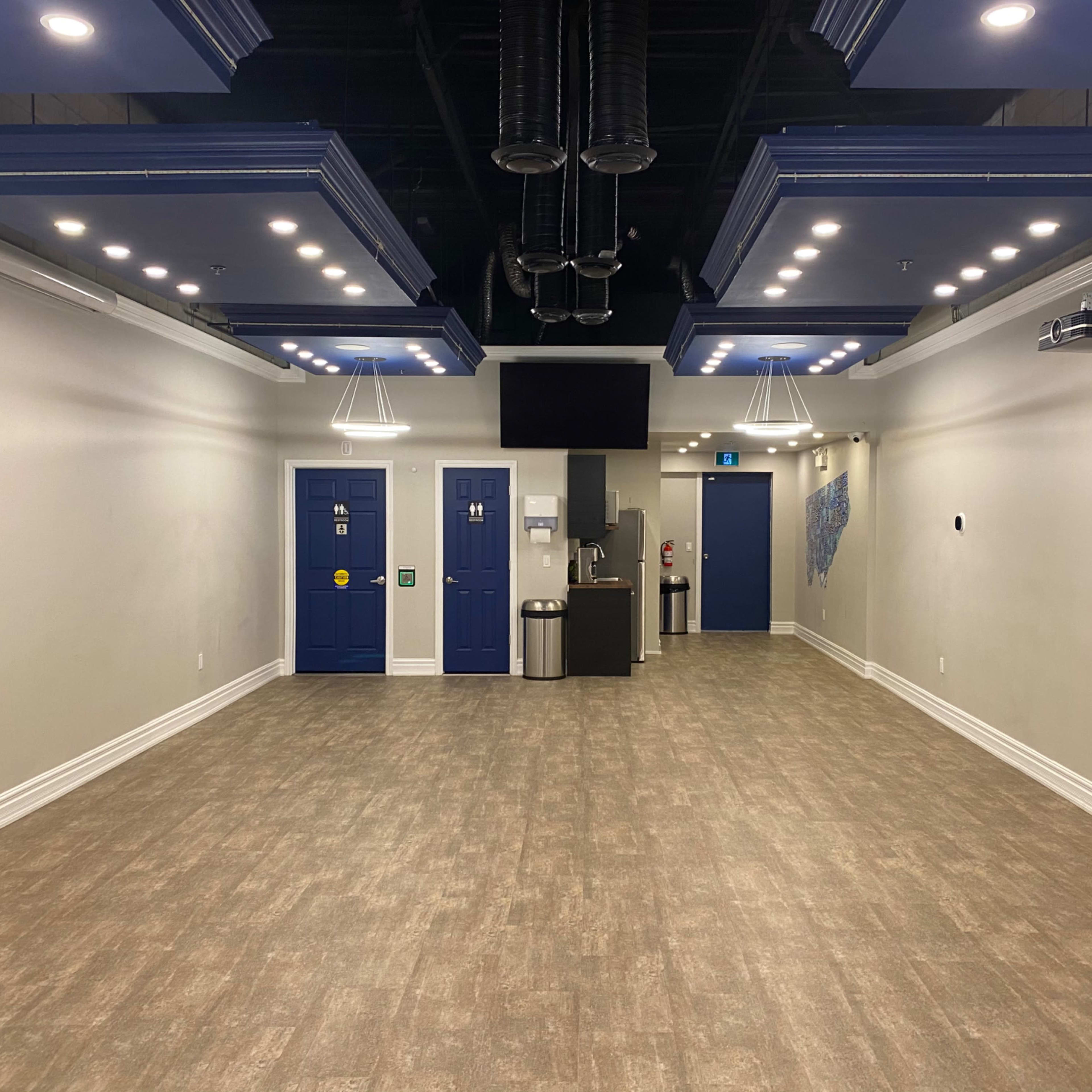 A spacious, well-lit interior room with blue doors and a kitchenette area on one side.