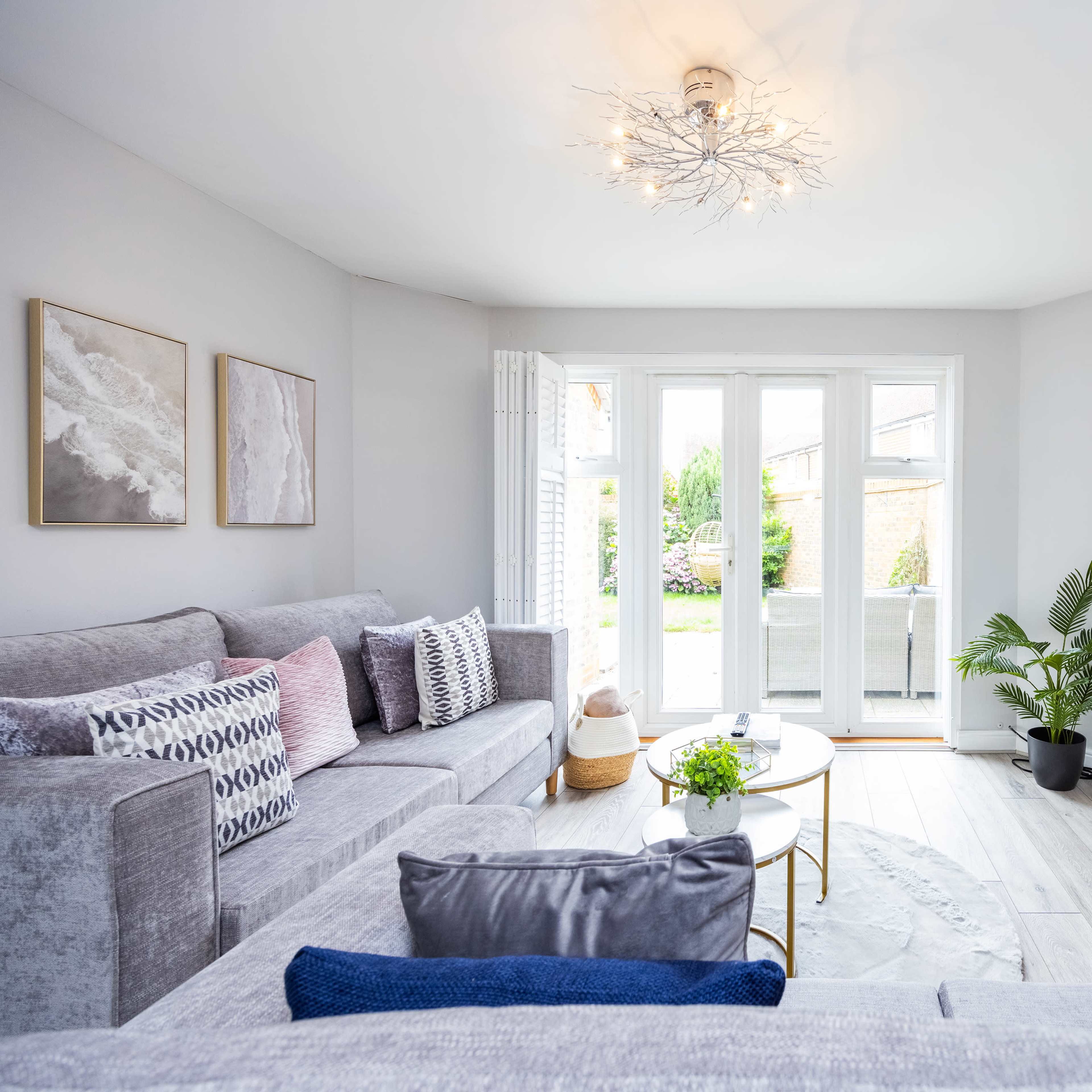 A modern living room features a gray sectional sofa, a round coffee table, and a television mounted on the wall, with large windows allowing natural light to fill the space.