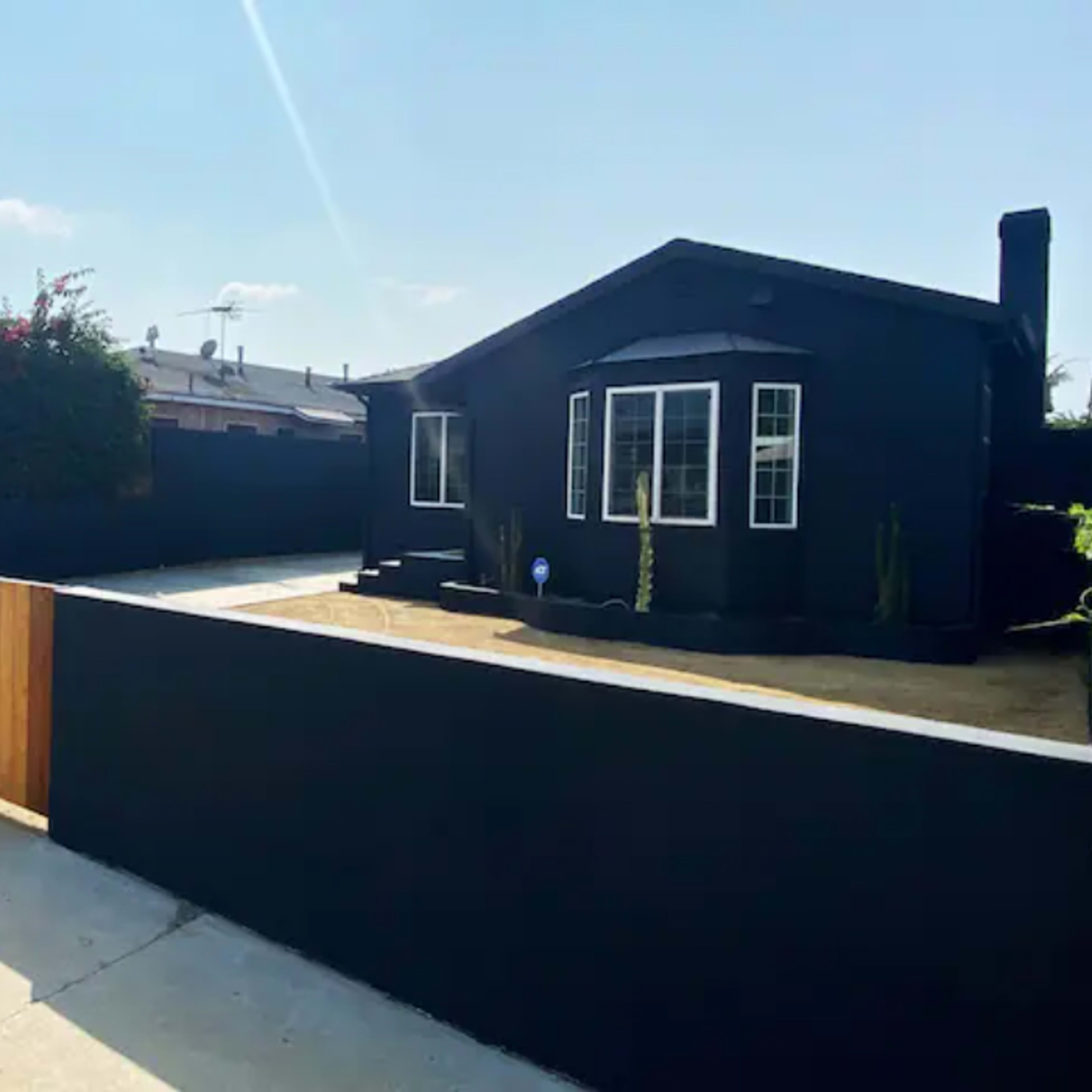A black-painted house behind a wooden fence with a landscaped front yard and a clear sky.