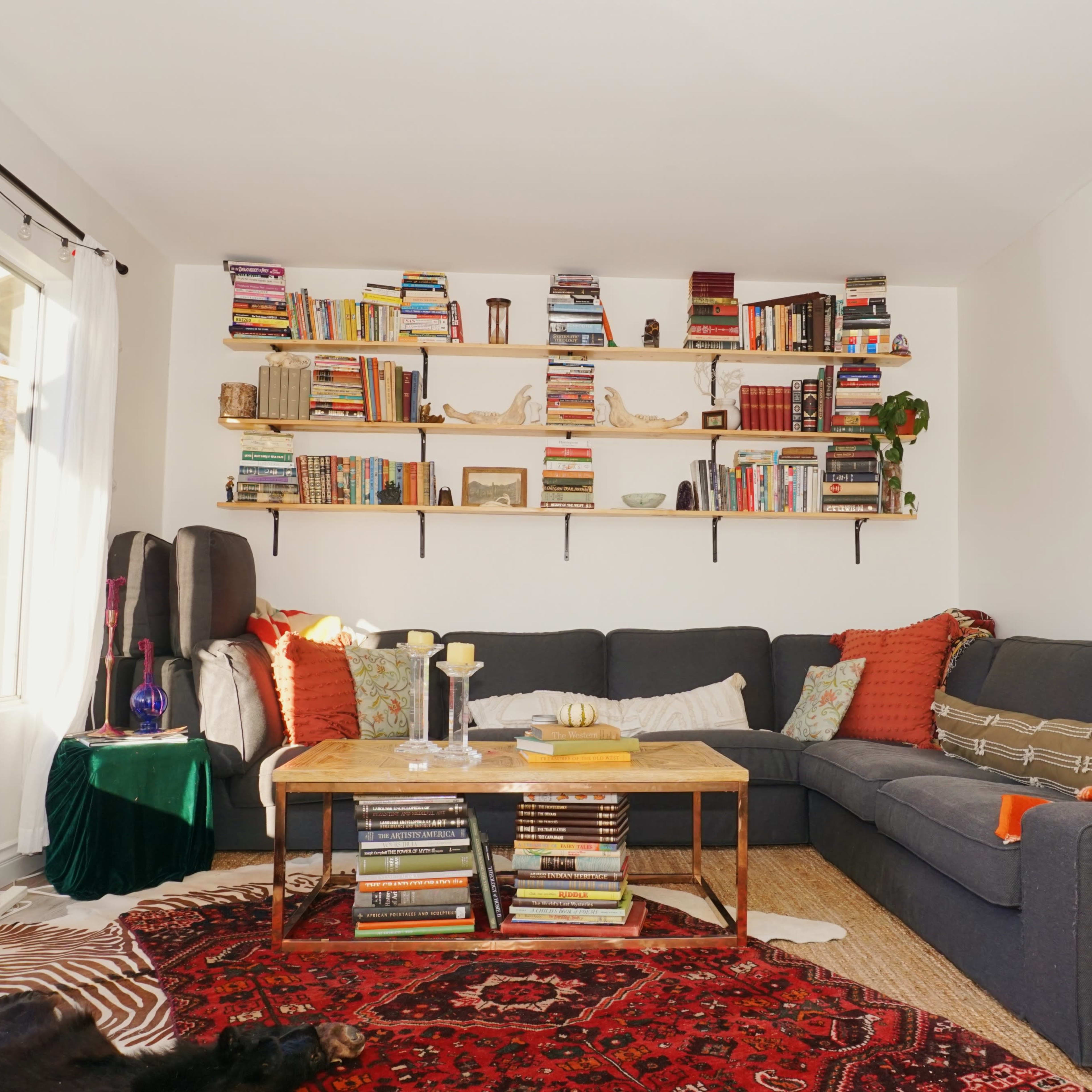 A cozy living room features a large sectional sofa adorned with colorful cushions, surrounded by bookshelves filled with books and decorative items.
