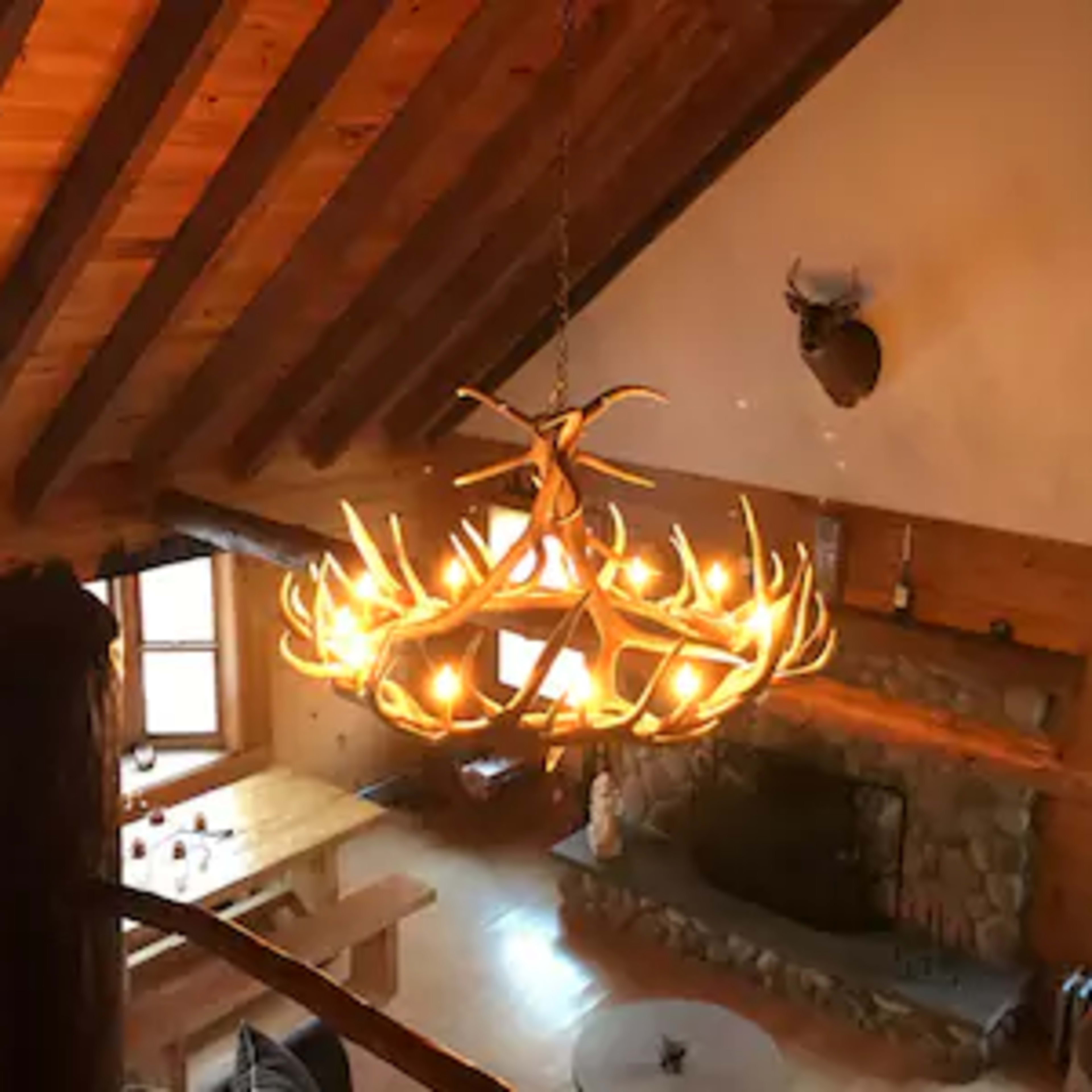 A rustic wooden living space with a large antler chandelier, a stone fireplace, and a dining table.