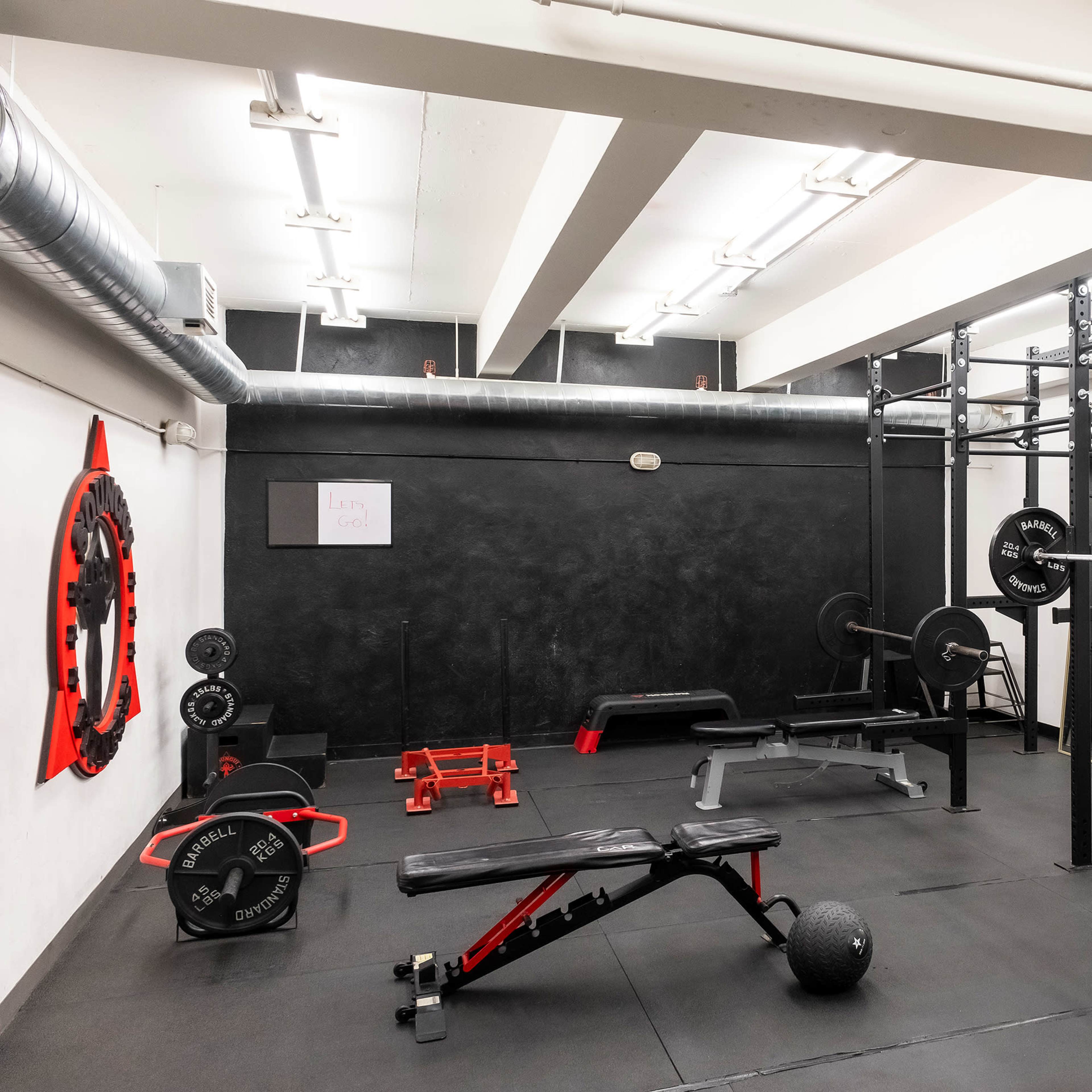 A gym interior featuring various weightlifting equipment, including a squat rack, benches, and free weights on a black rubber floor.