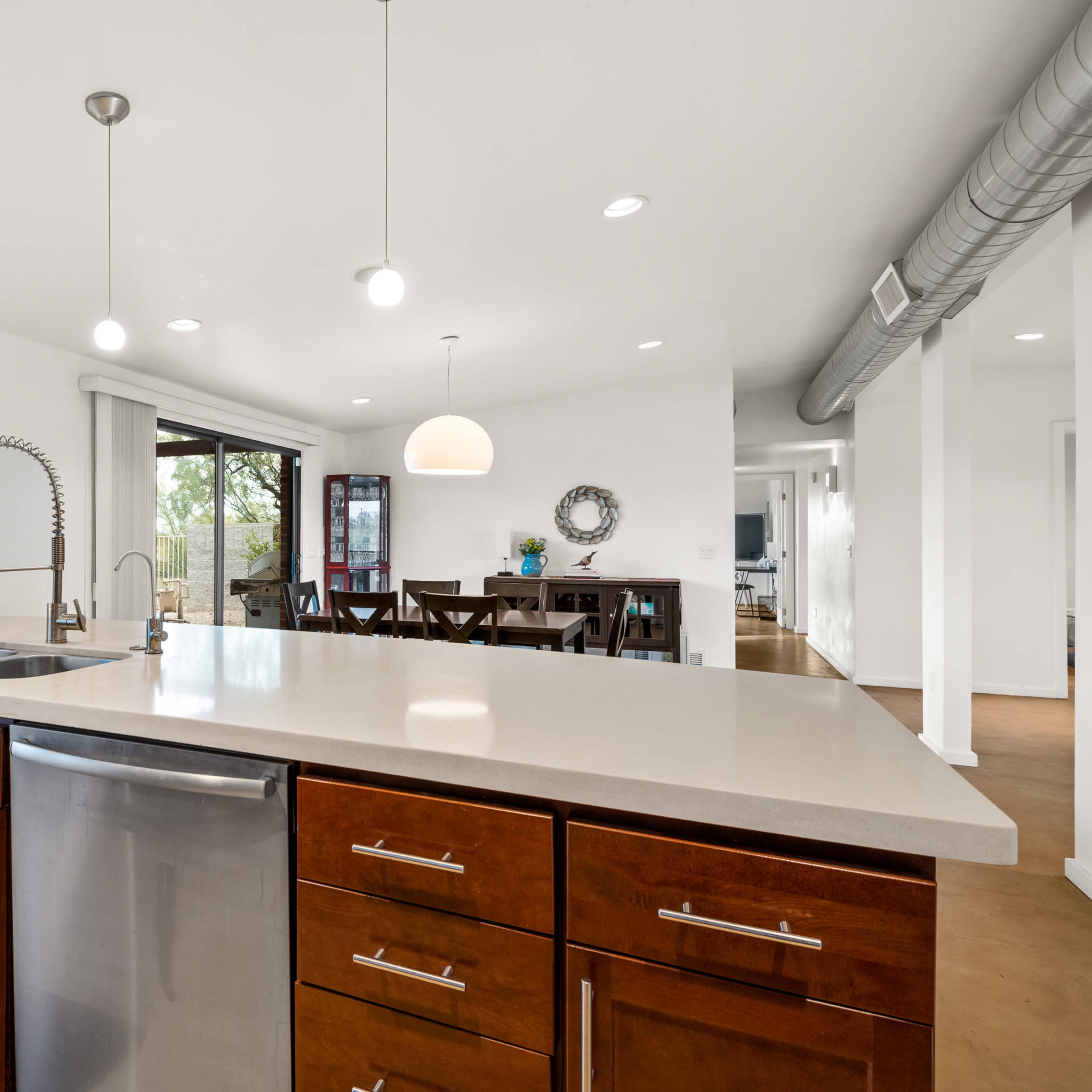A modern kitchen features wooden cabinets, a stainless steel dishwasher, and an island with a sink and pendant lighting.
