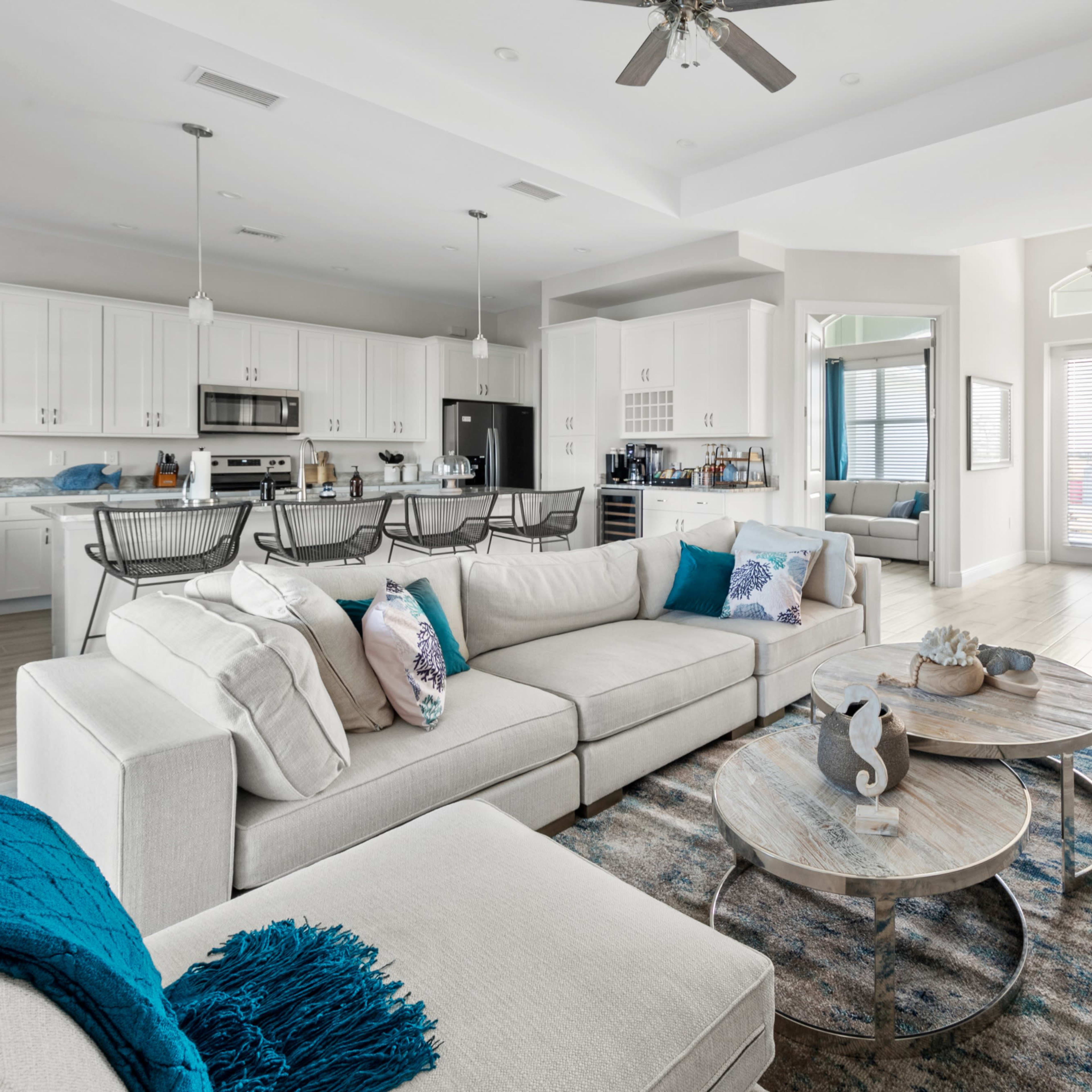 A modern living room with a large sectional sofa, circular wooden coffee tables, and a kitchen area visible in the background.