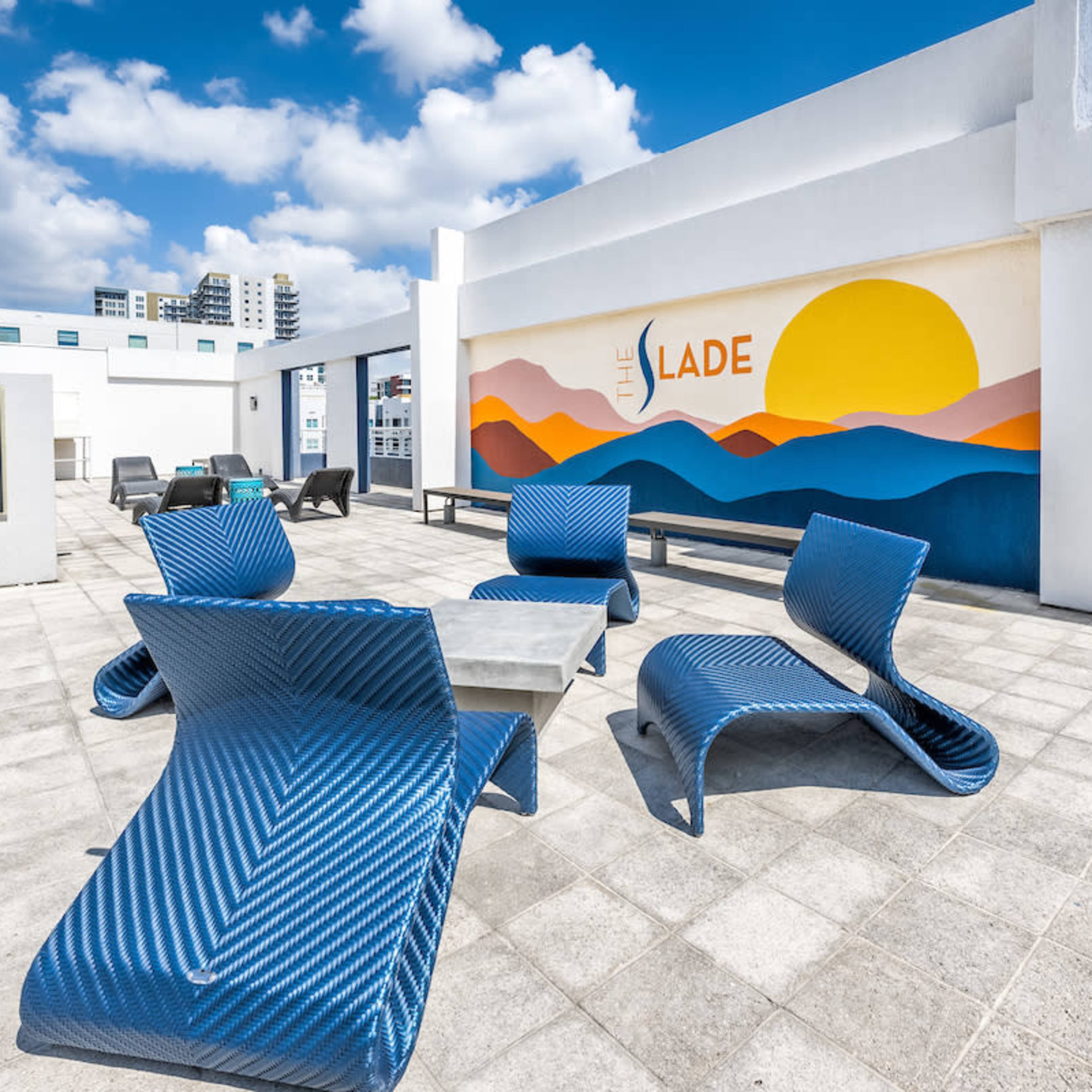 The rooftop terrace features blue lounge chairs and a mural depicting a sunset over mountains.