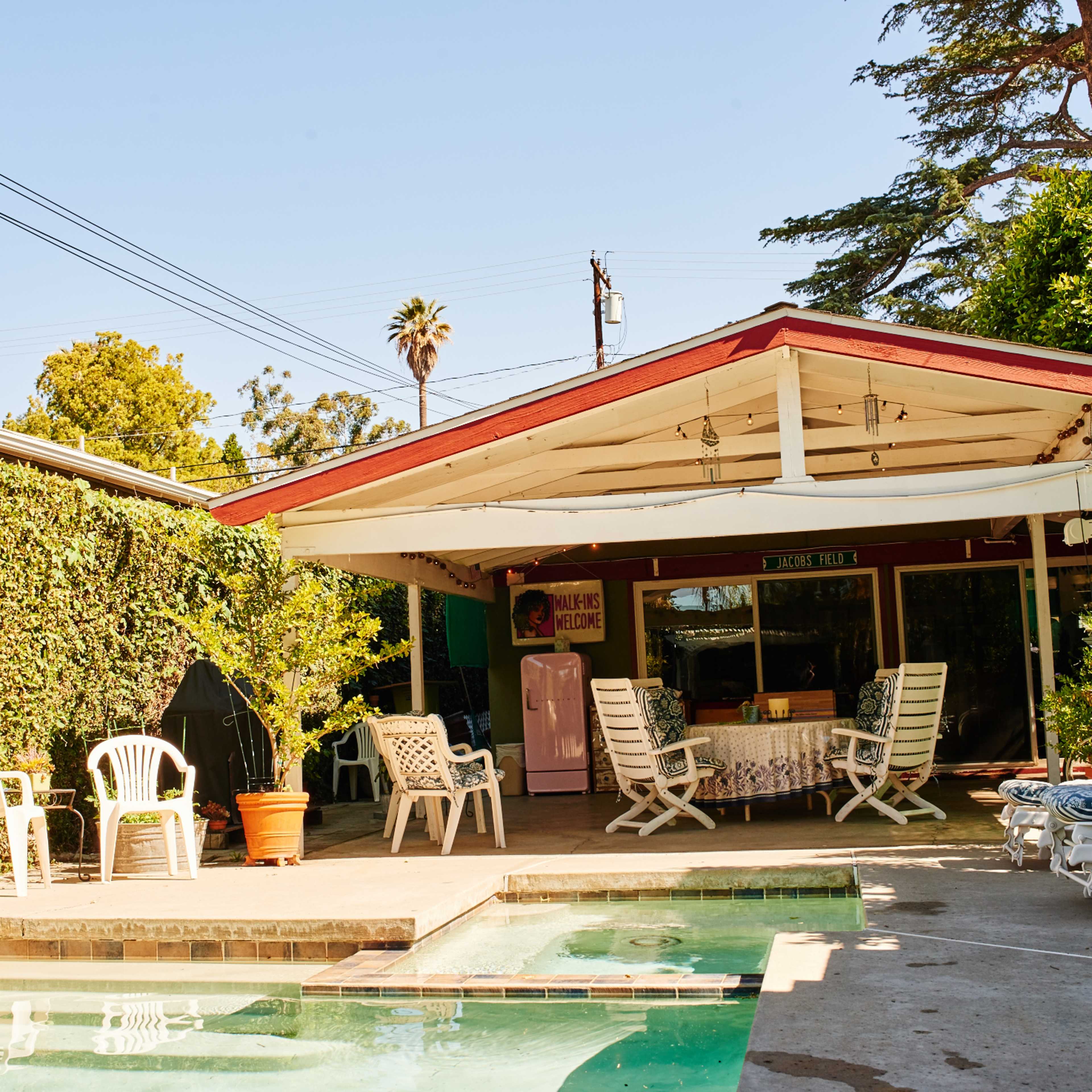 A backyard patio features a pool, seating area, and a shaded dining space under a slanted roof.