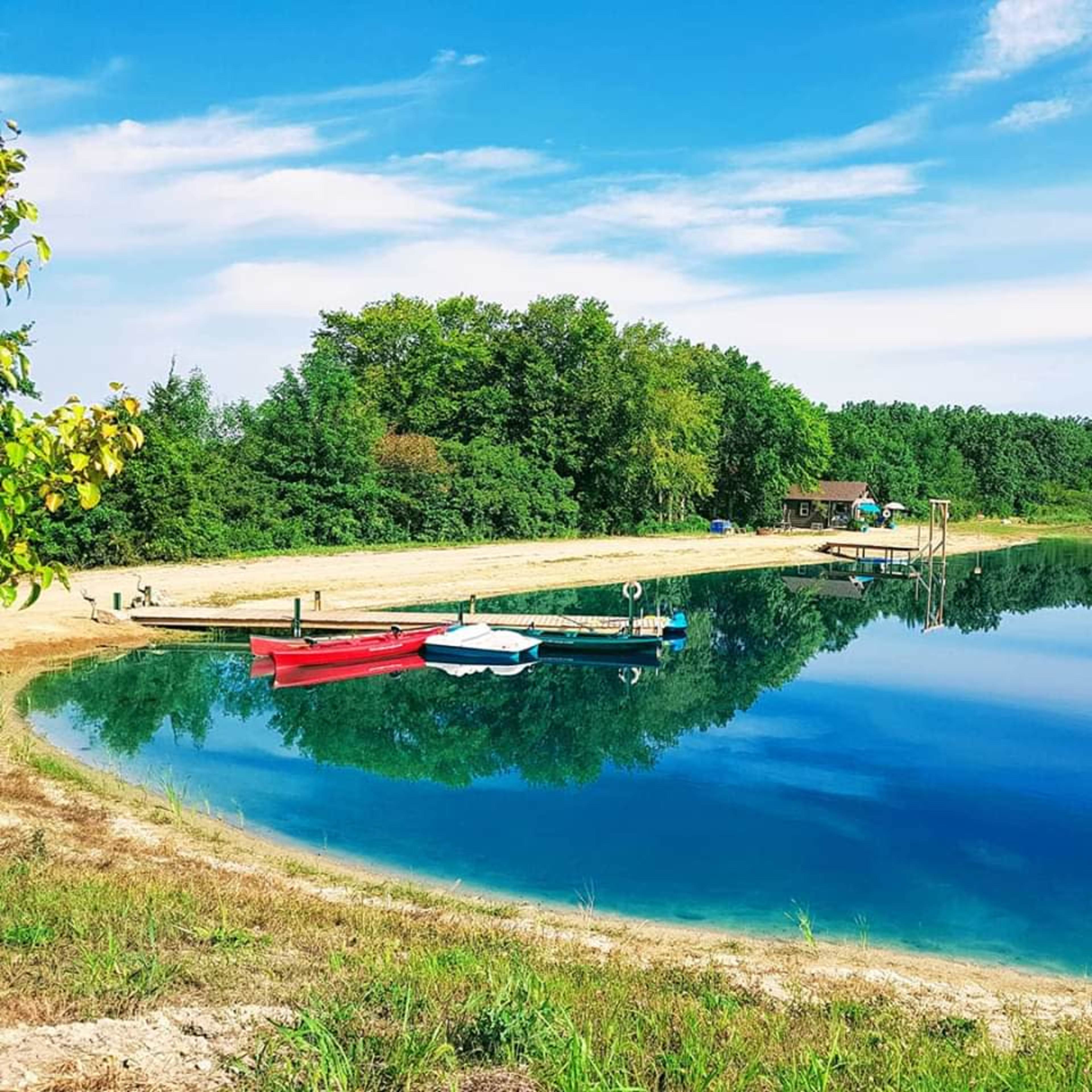 A calm lake reflects the surrounding trees and sky, with several boats docked along the shoreline.