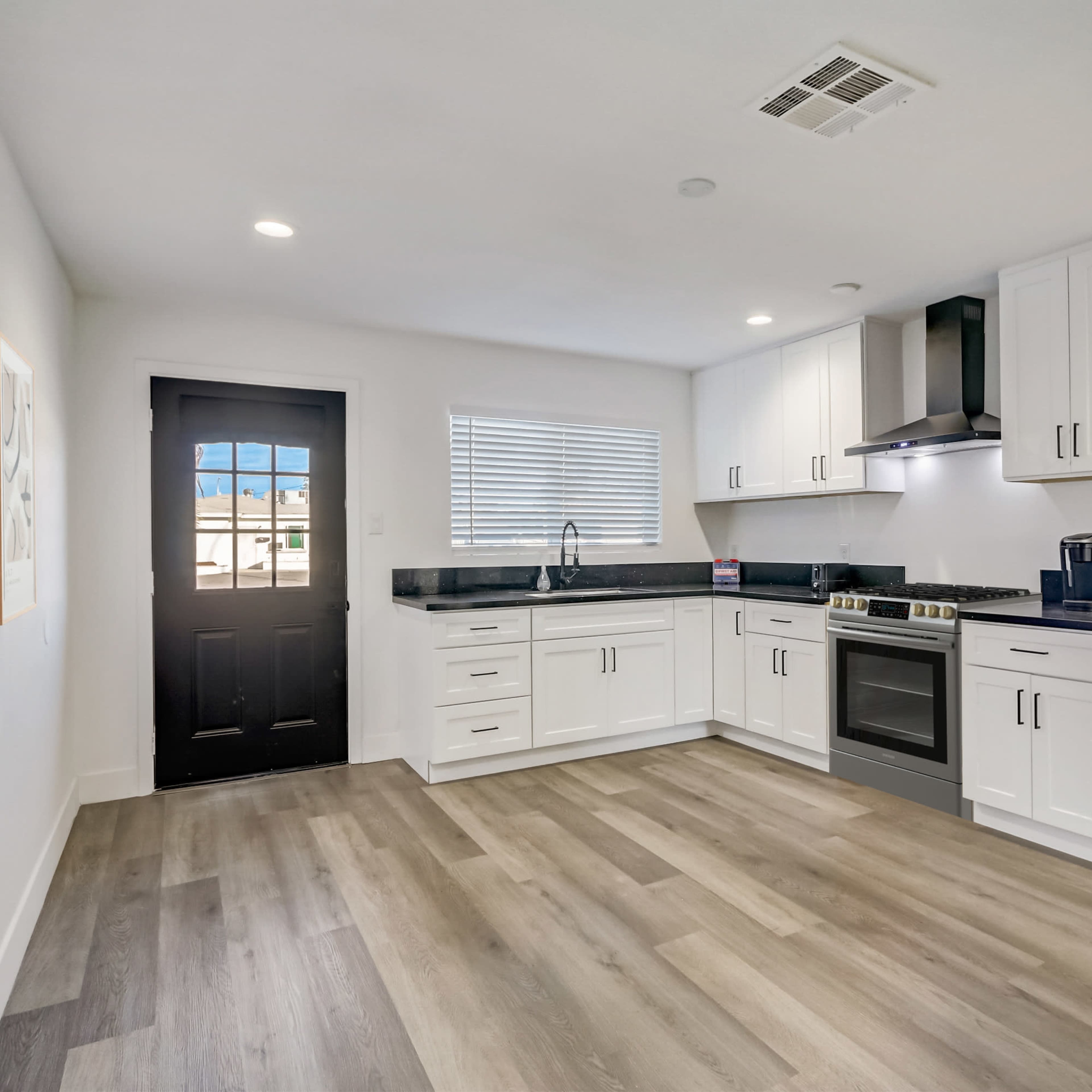 A modern kitchen with white cabinets, a black stove, and a door leading outside.