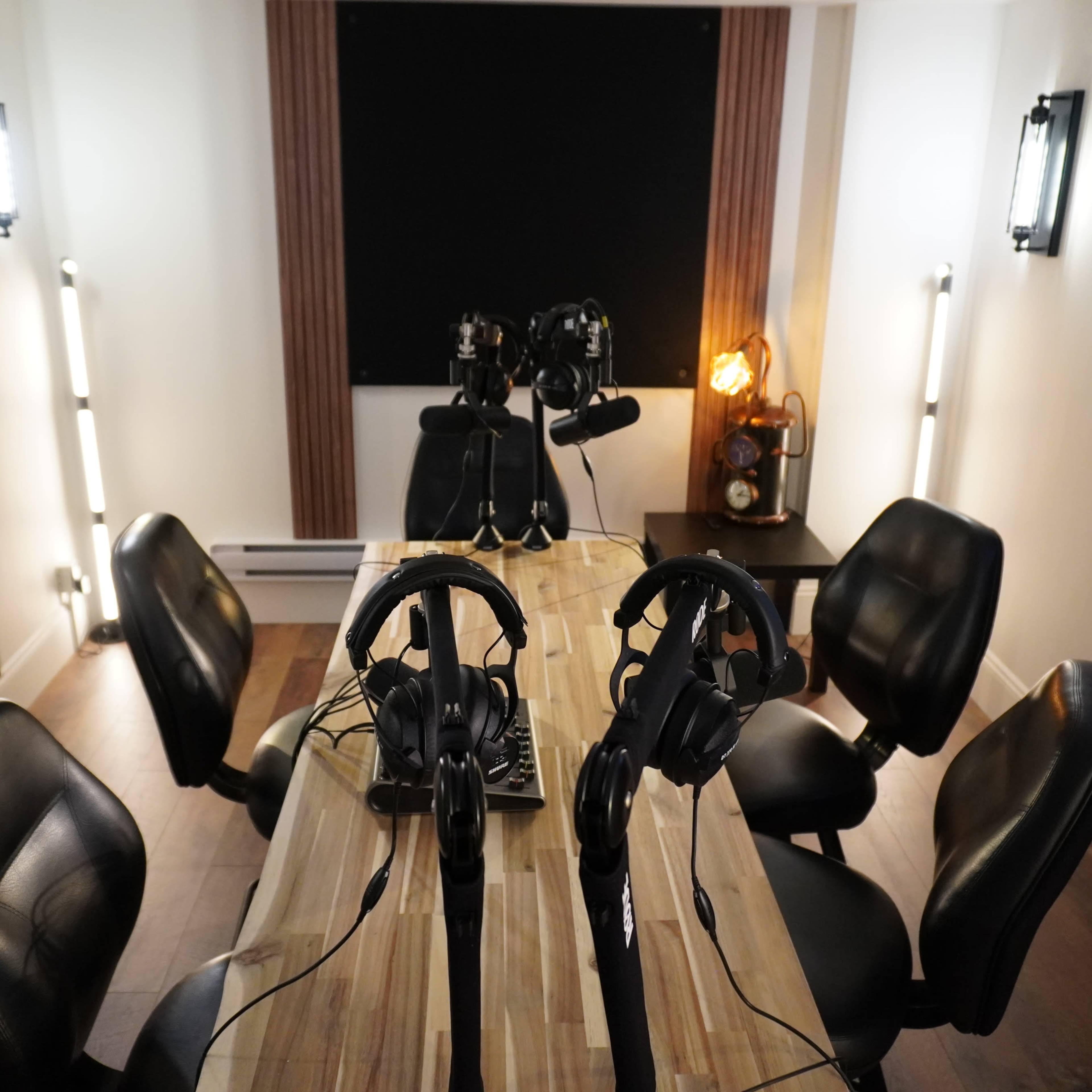 A small soundproof studio with a wooden table, four black chairs, and two microphones set up for recording.