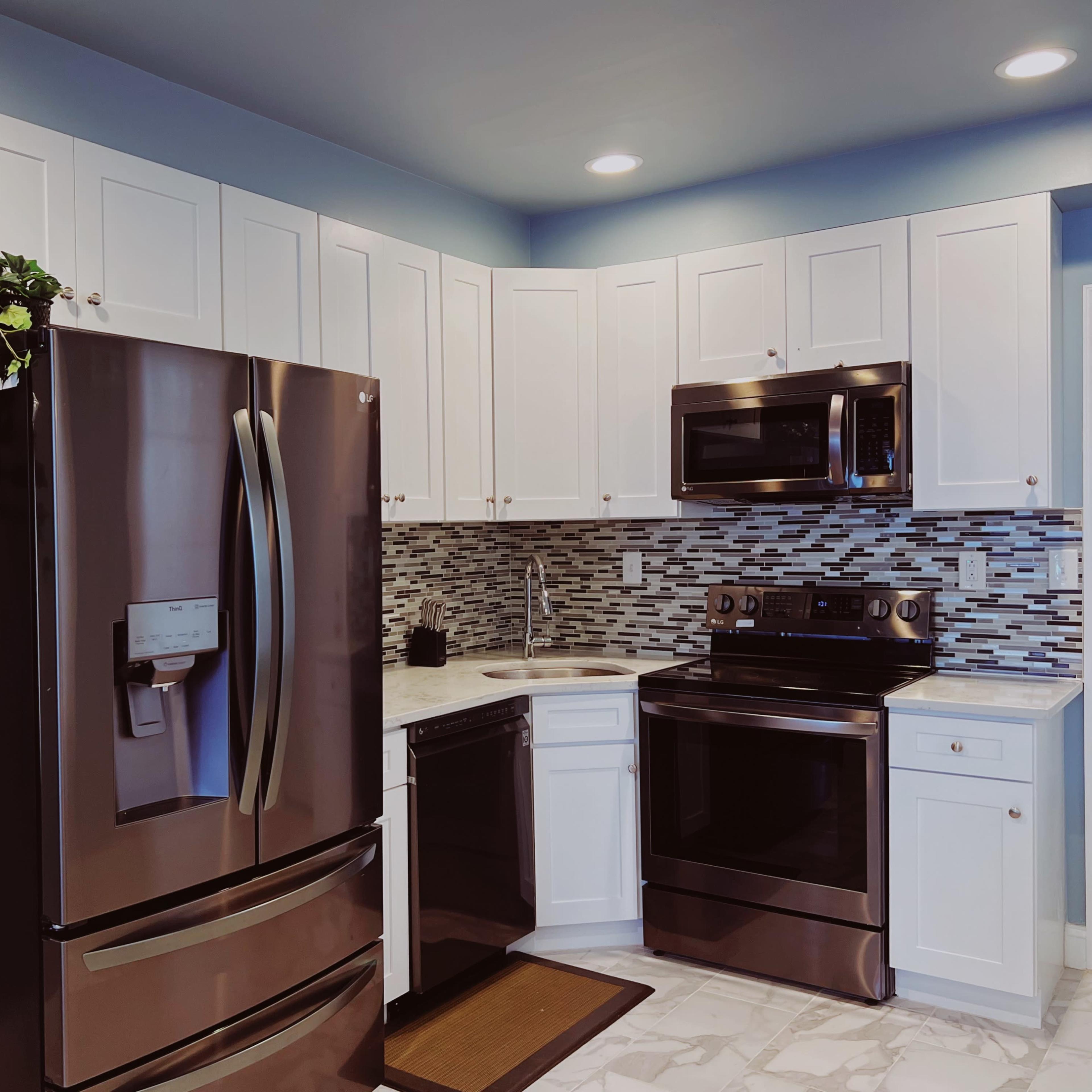 A modern kitchen featuring stainless steel appliances, white cabinetry, and a tiled backsplash.