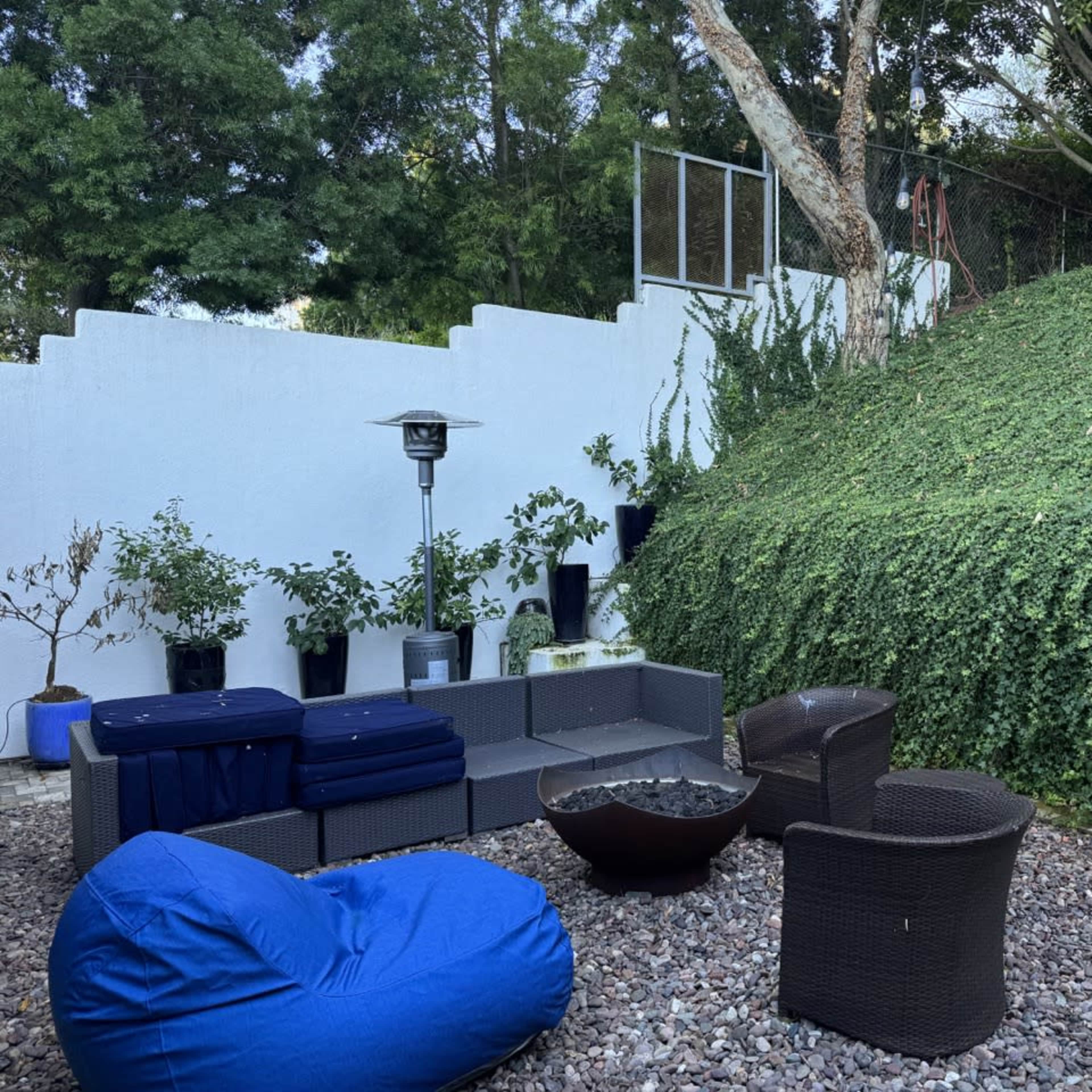 The outdoor space features a seating area with a fire pit surrounded by garden plants and a hillside covered in greenery.