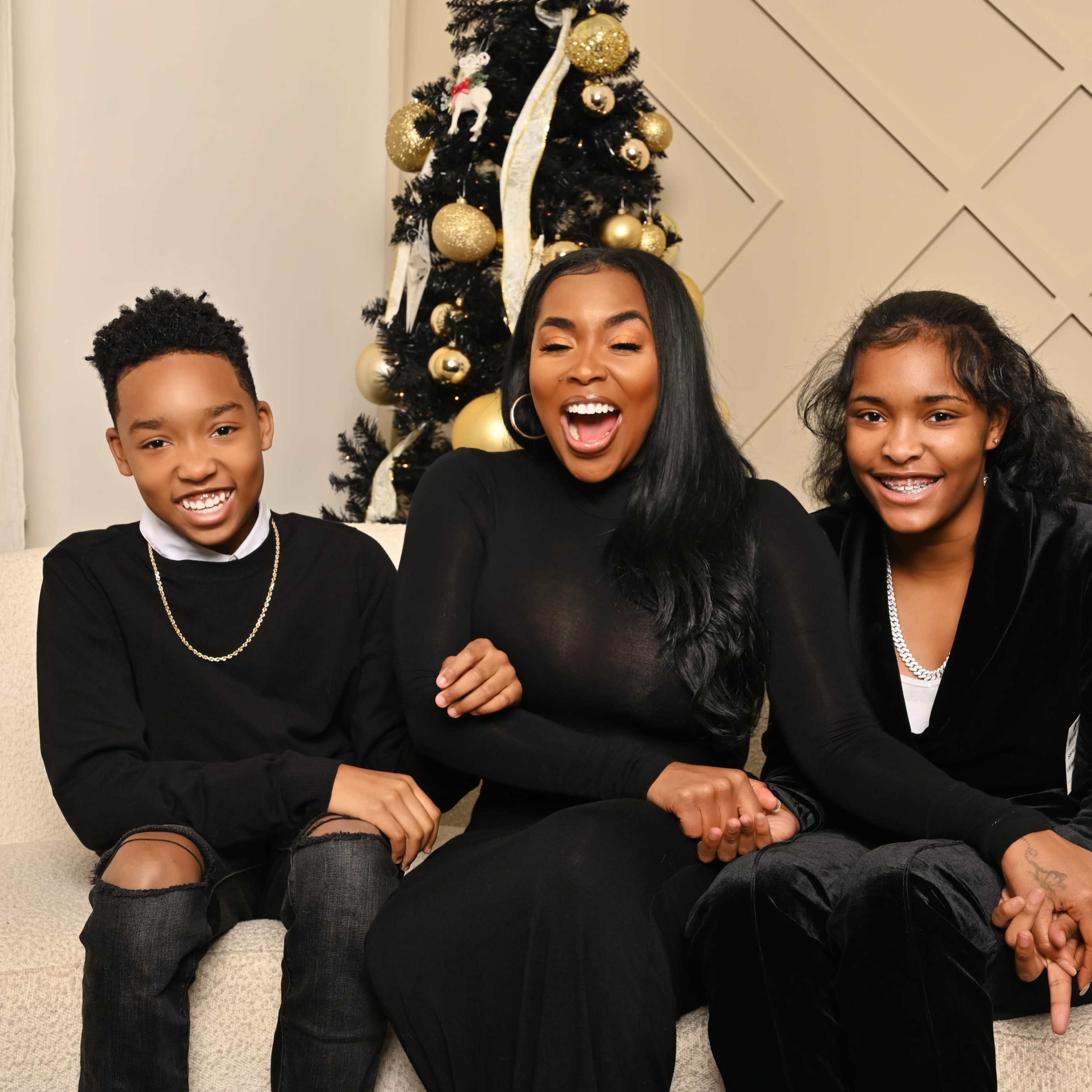 A woman and two children are sitting on a sofa in front of a decorated Christmas tree.