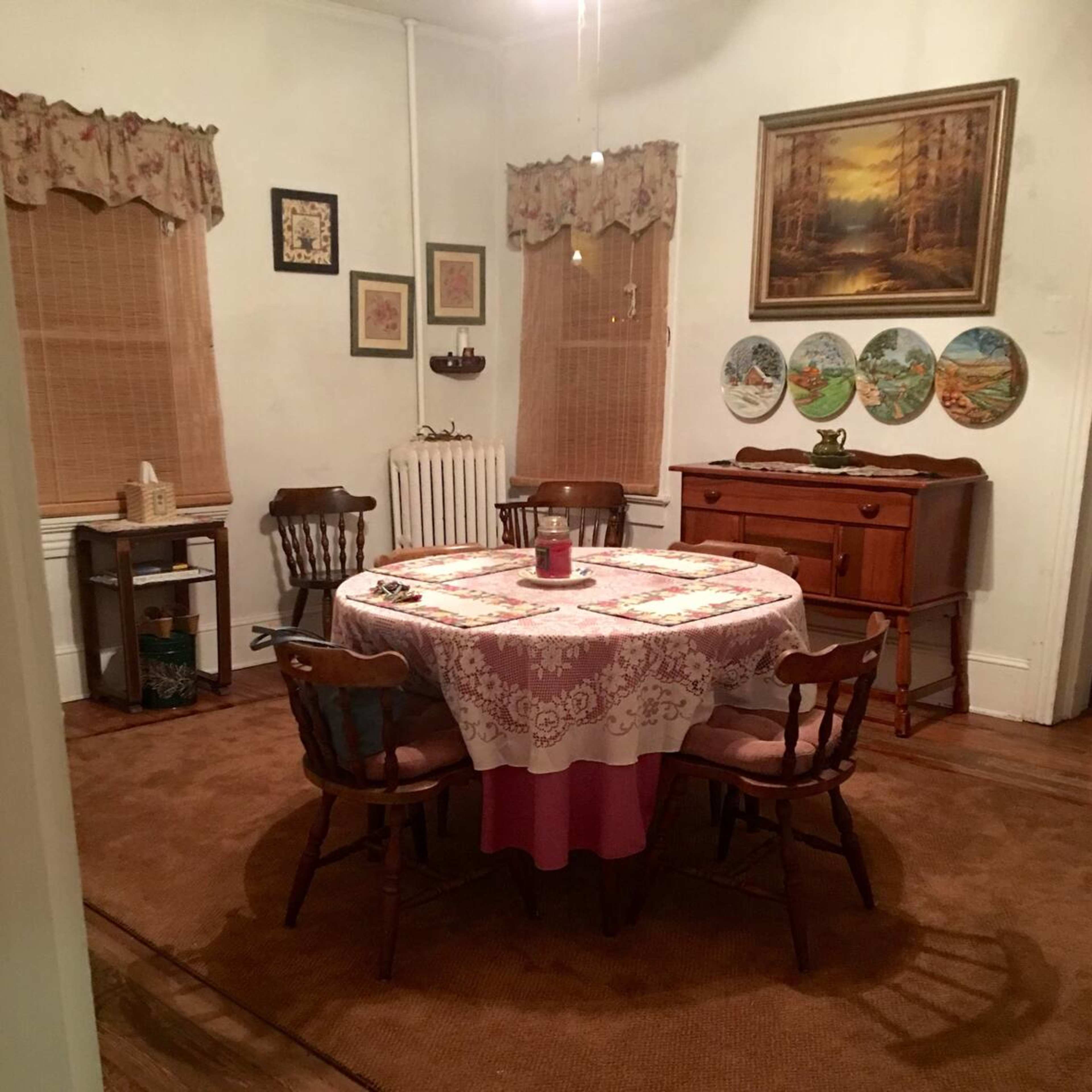 A cozy dining room with a round table set in the center, surrounded by wooden chairs, and adorned with framed artwork and decorative plates on the walls.