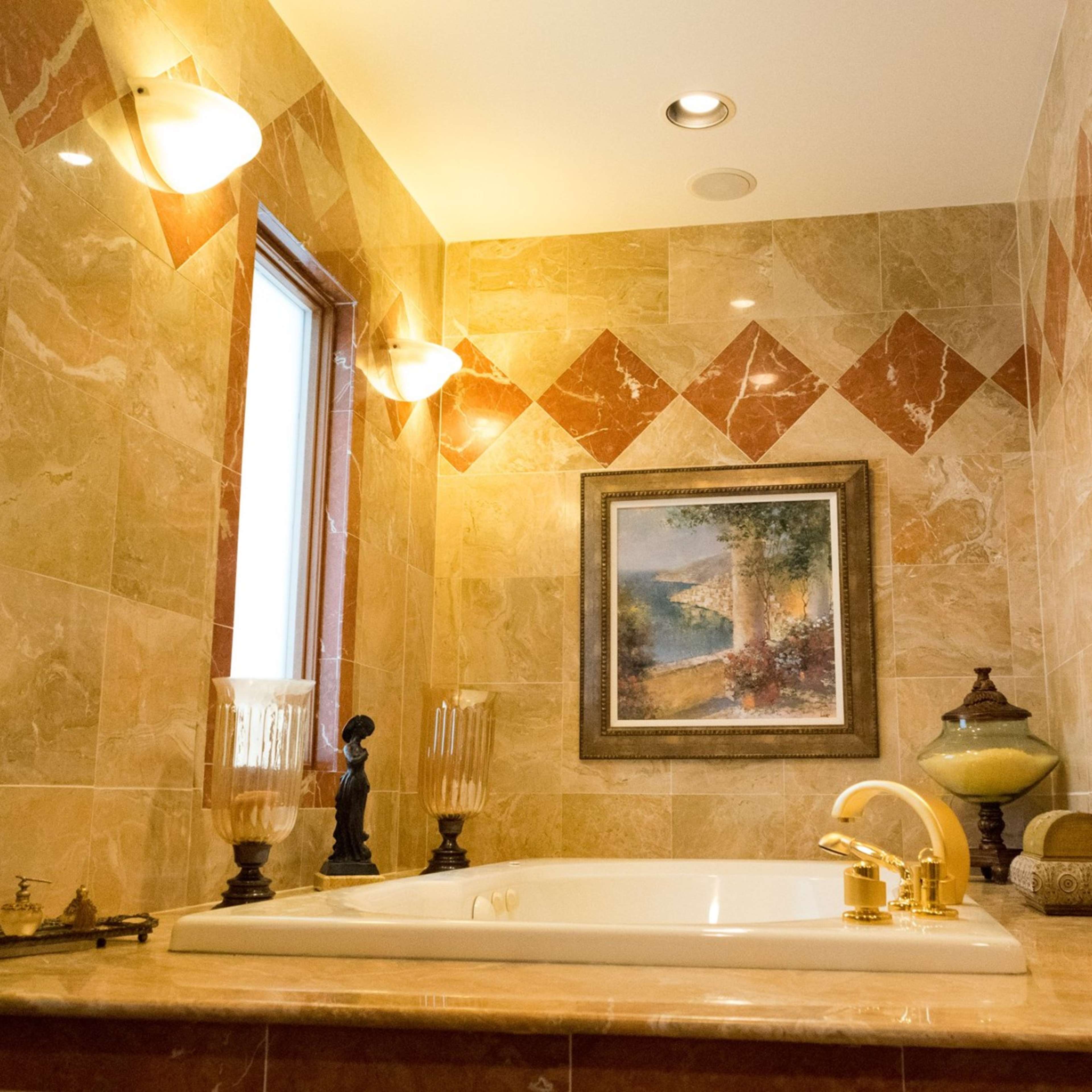 A bathroom with marble walls, a large bathtub, and decorative elements including a painting and candles.