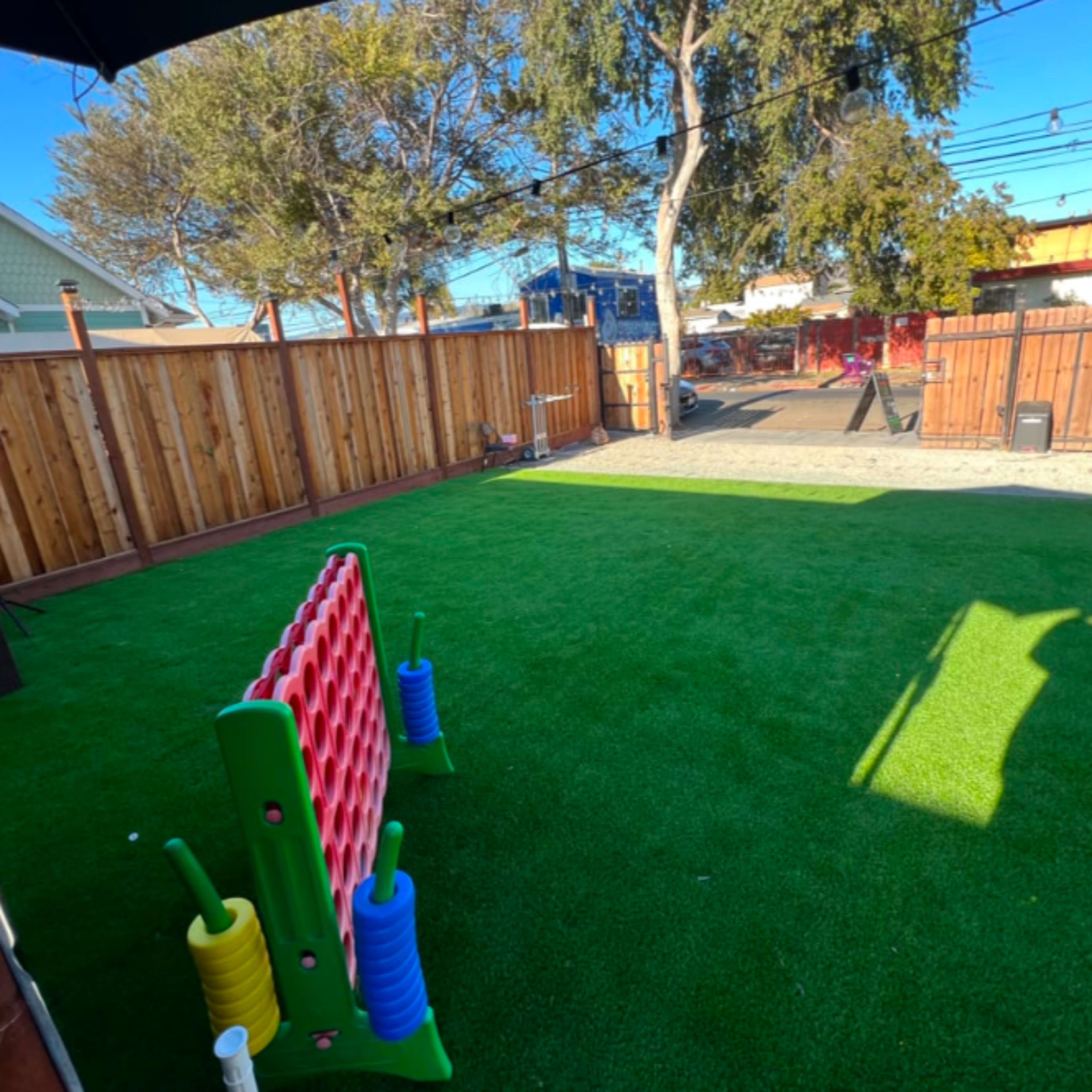 A fenced backyard features artificial grass, a brightly colored play structure, and a parked car nearby.