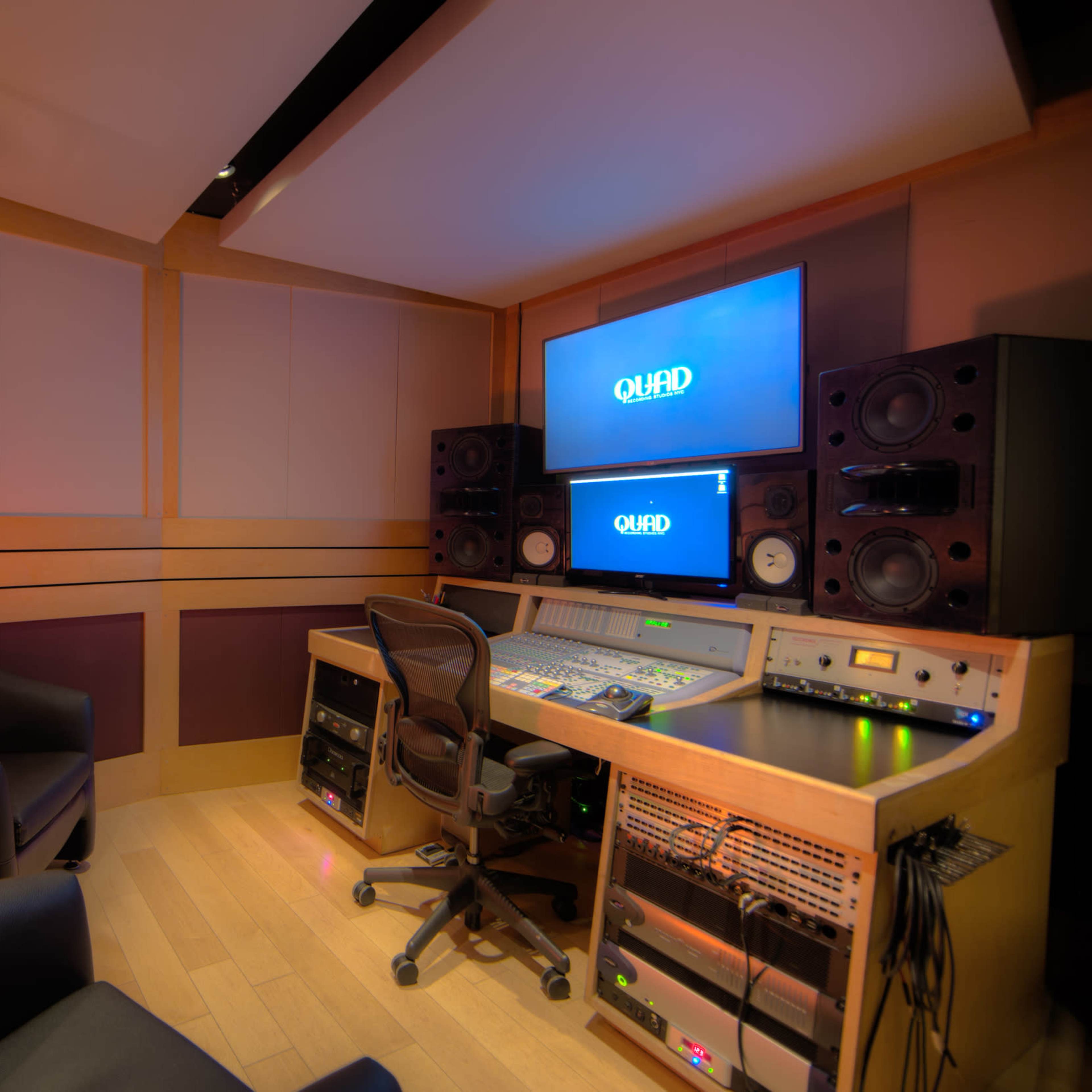 A recording studio featuring a control desk with audio equipment, large speakers, and a computer monitor, alongside two black chairs and a salt lamp in a cozy corner.