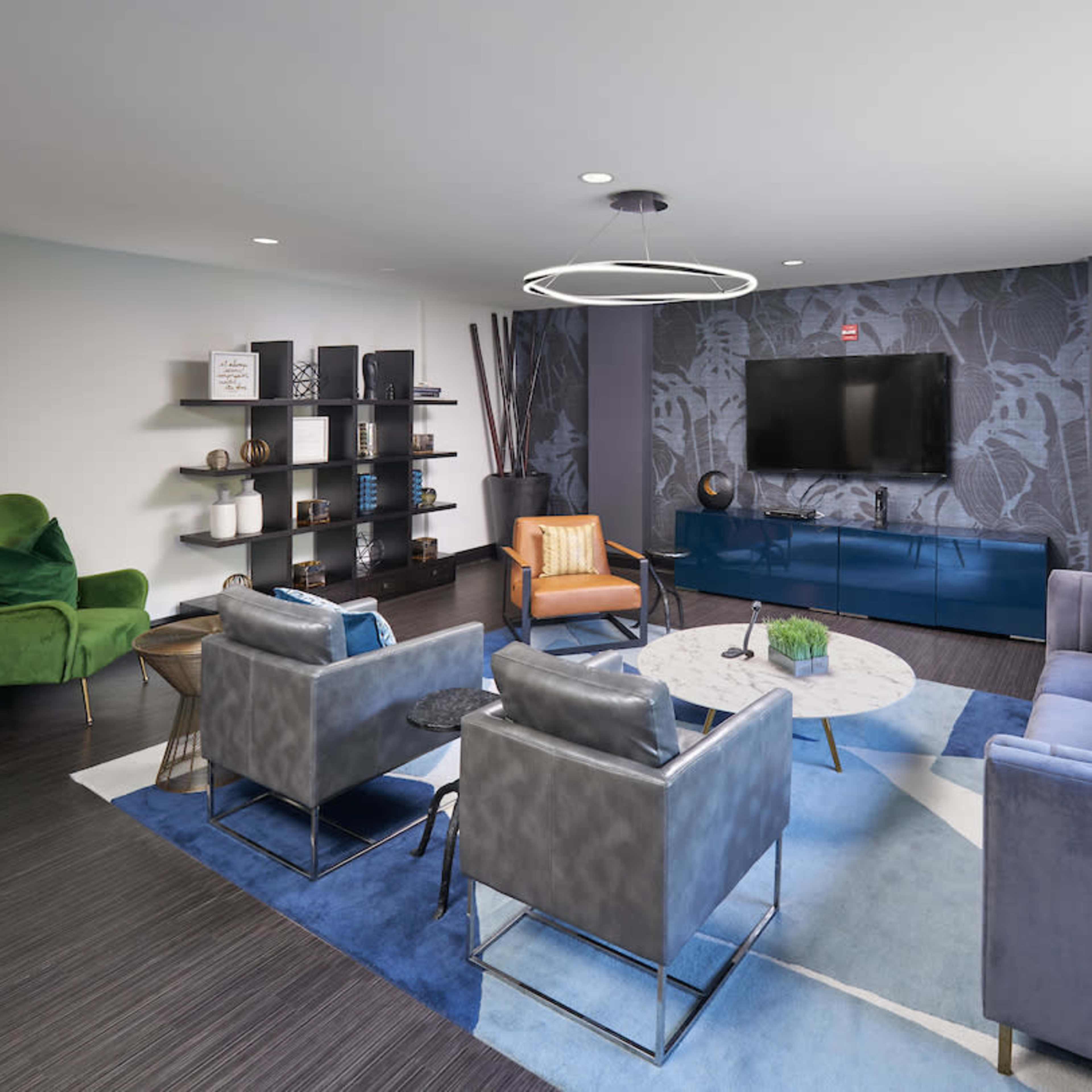 A modern lounge area features a blue and gray color scheme with a television mounted on the wall, stylish seating, and decorative shelves.