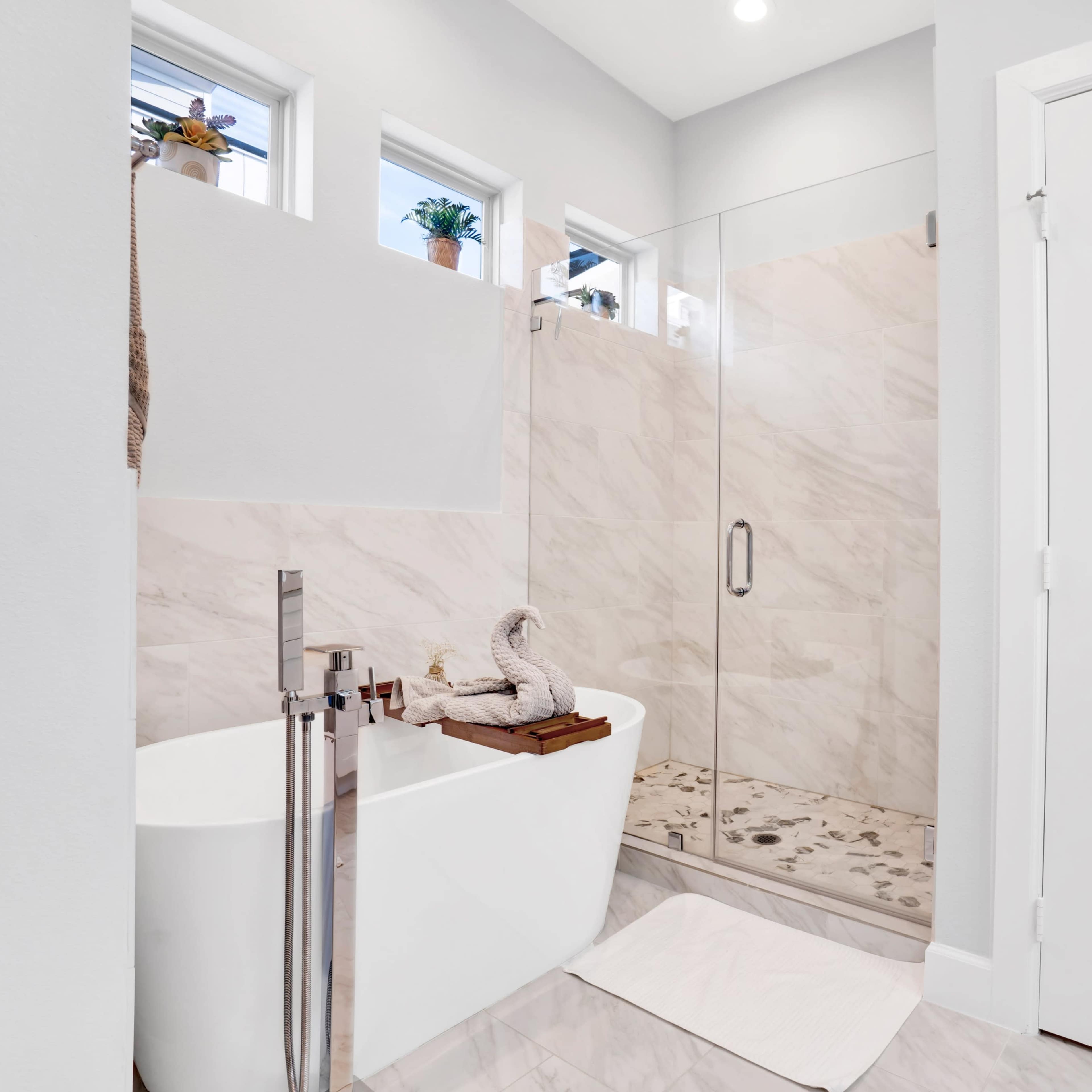 A modern bathroom with a freestanding white bathtub, a glass shower enclosure, and light-colored marble walls and flooring.