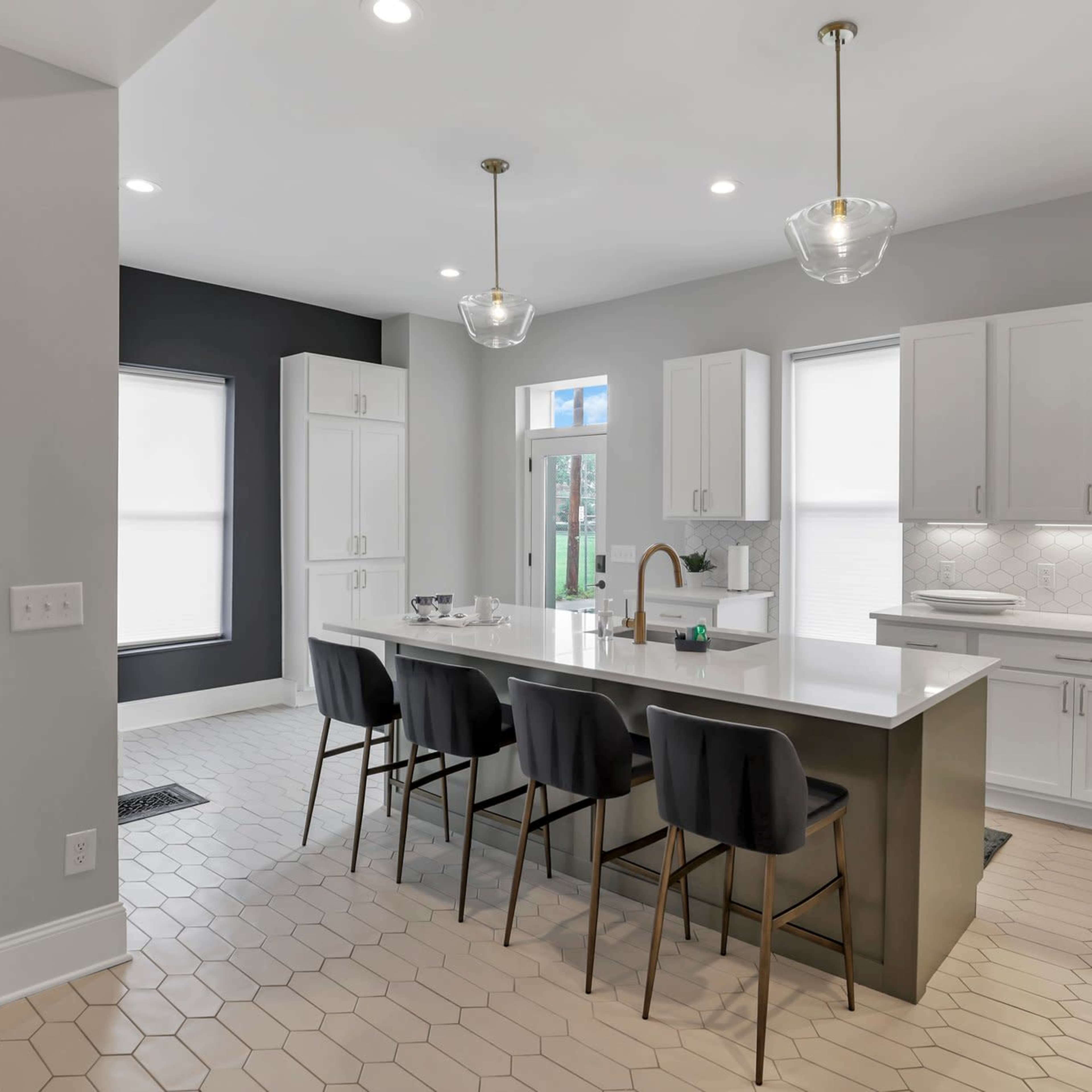 A modern kitchen features a large island with seating and white cabinetry, complemented by hexagonal floor tiles and natural light from nearby windows.