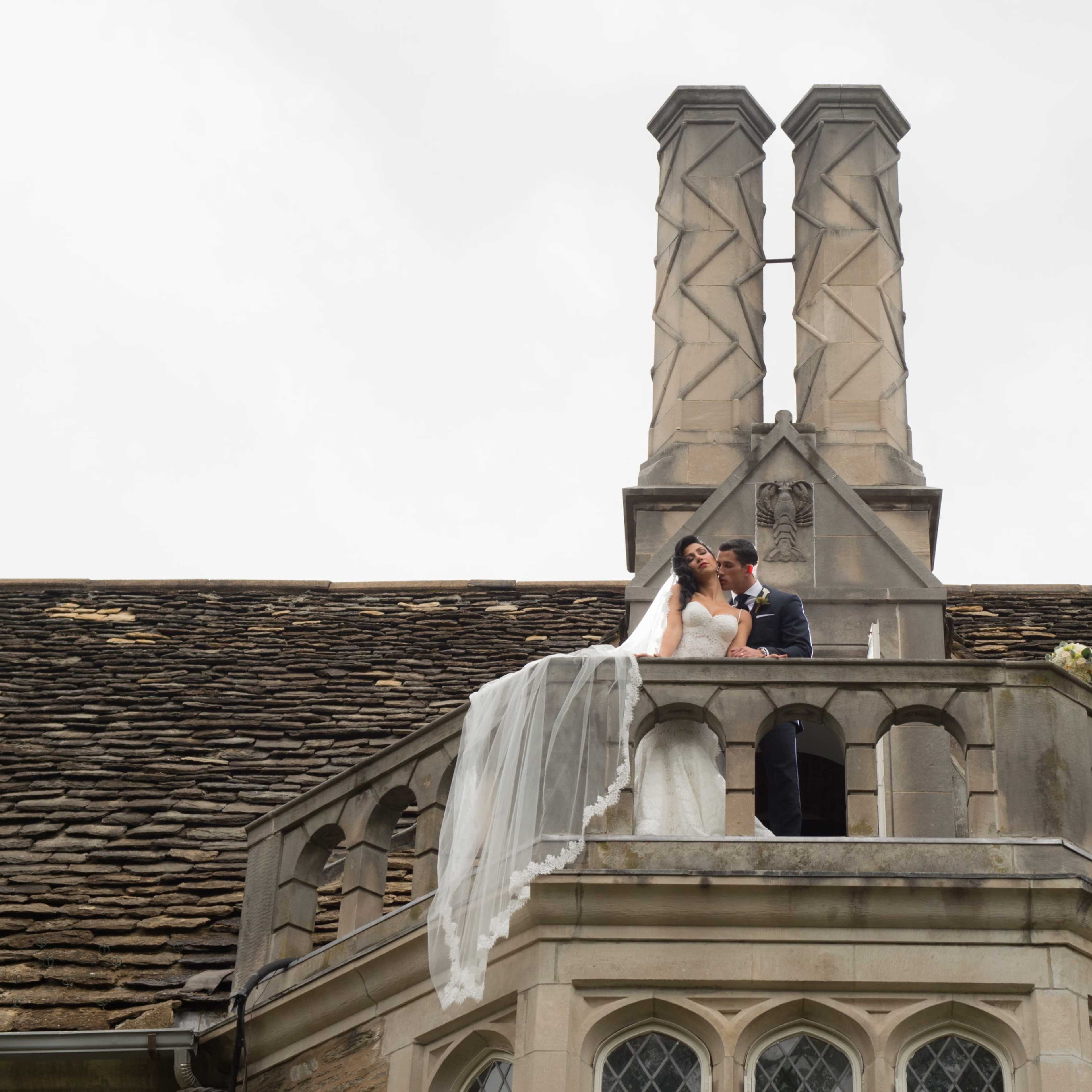 A couple embraces on a balcony adorned with a chimney at a historic building.