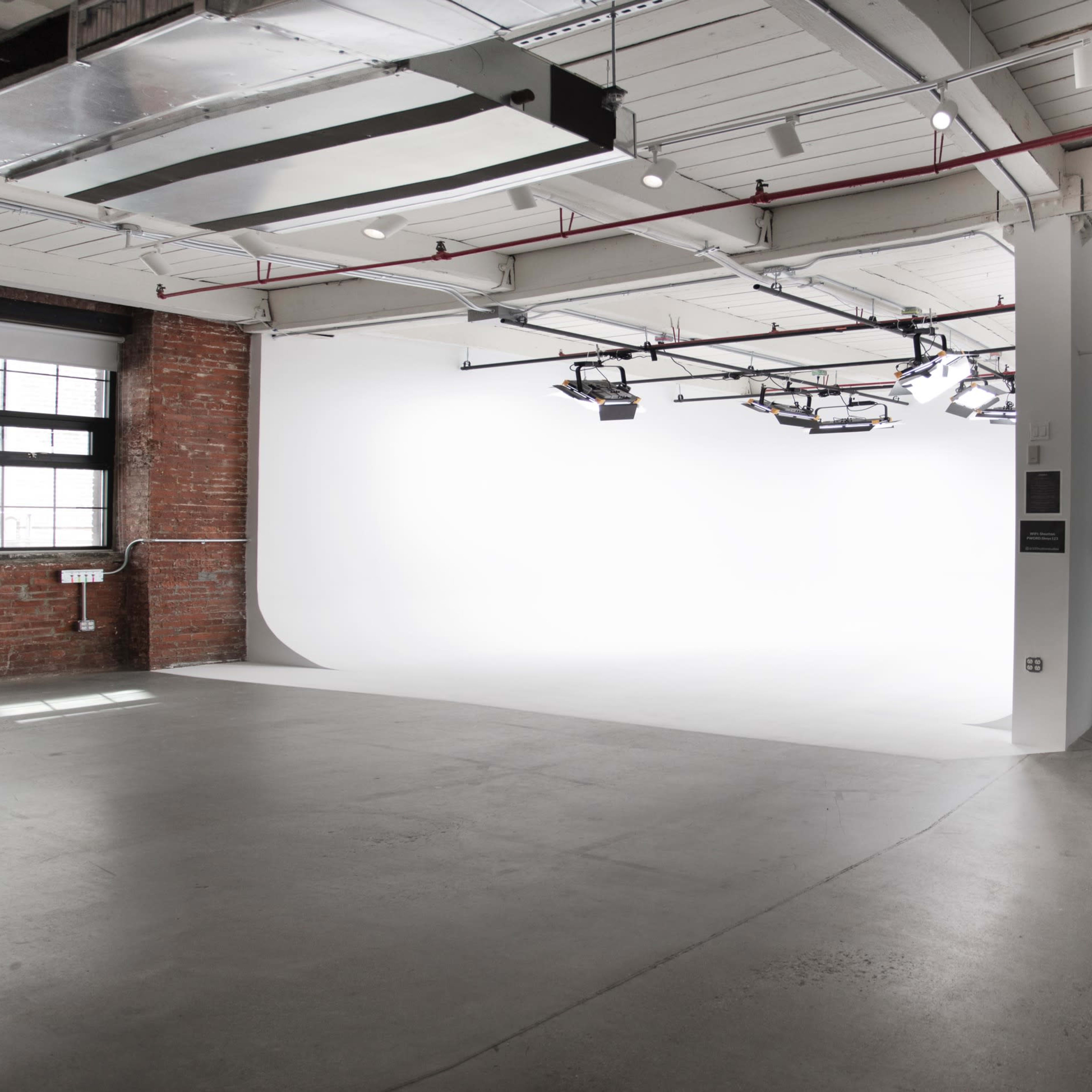 A spacious, minimalist studio with exposed brick walls, concrete flooring, and a large white backdrop.