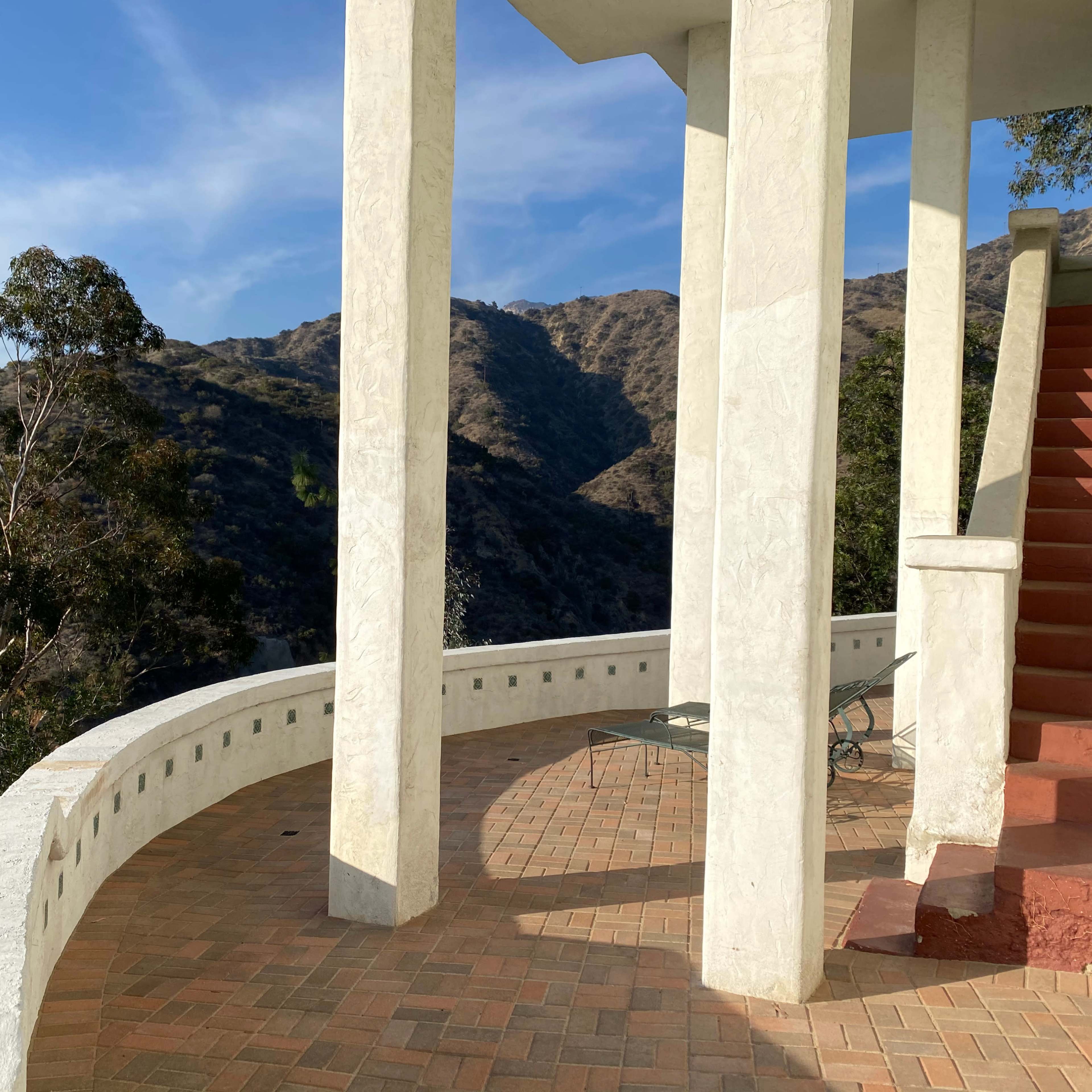 A terrace with white columns and a staircase, overlooking a mountainous landscape under a clear blue sky.