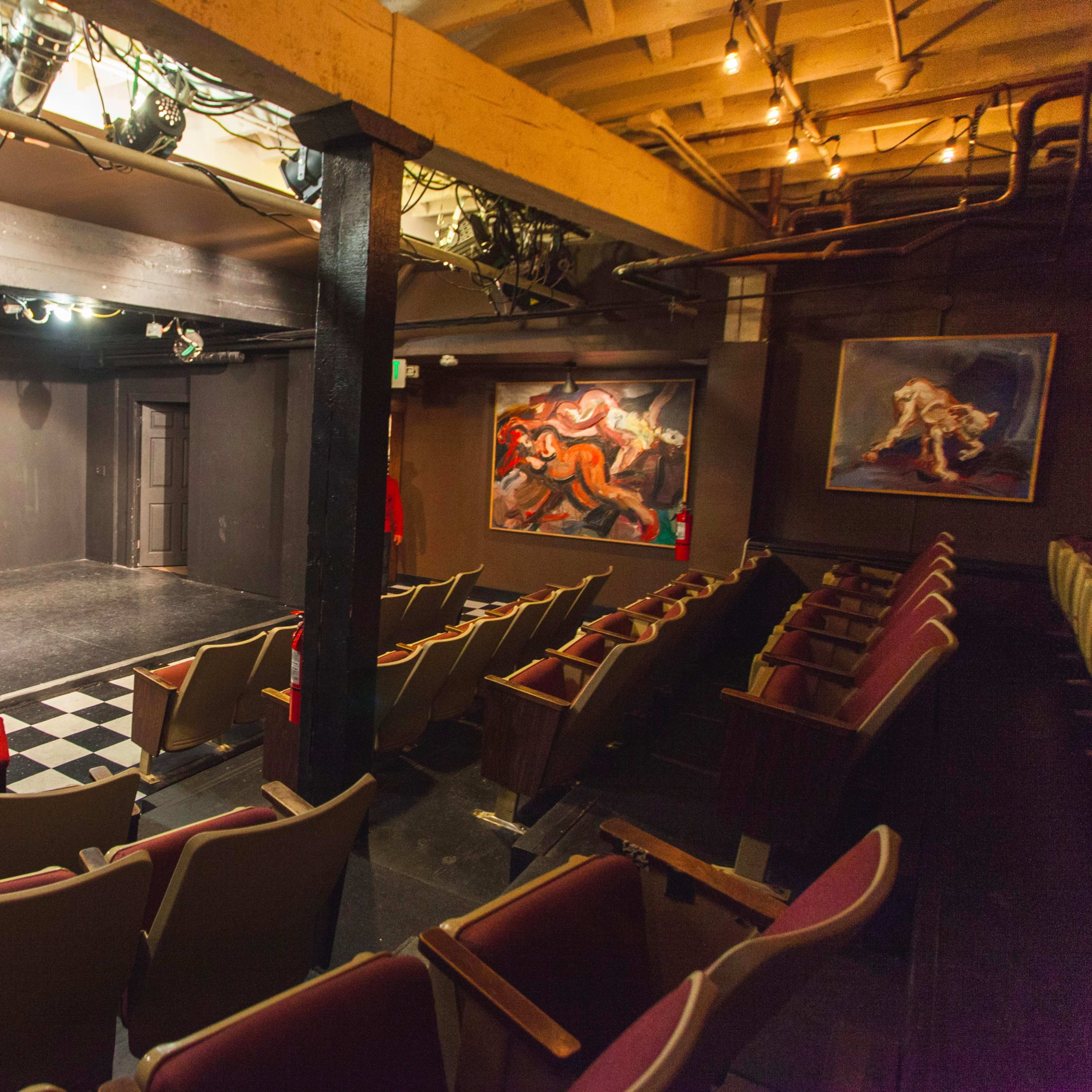 A small theater with a dimly lit stage and an empty audience area featuring rows of seats.