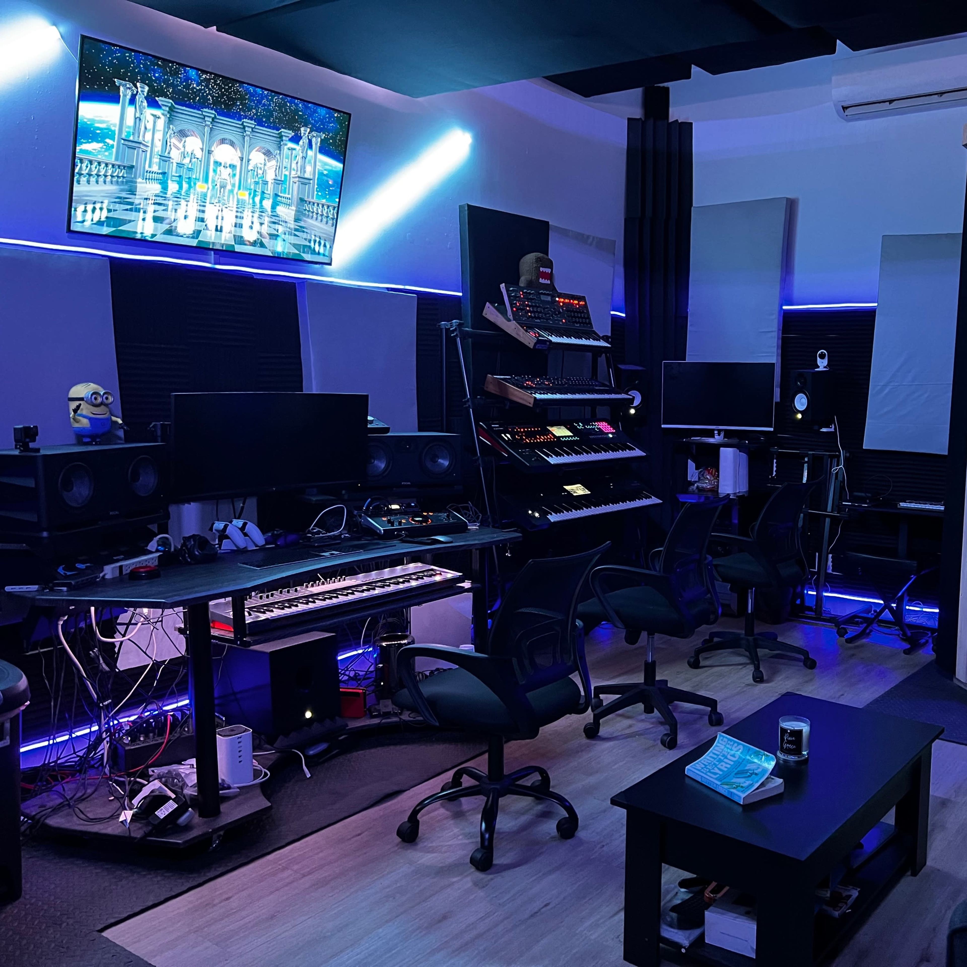 A modern recording studio equipped with multiple computer monitors, musical instruments, and a vocal booth.