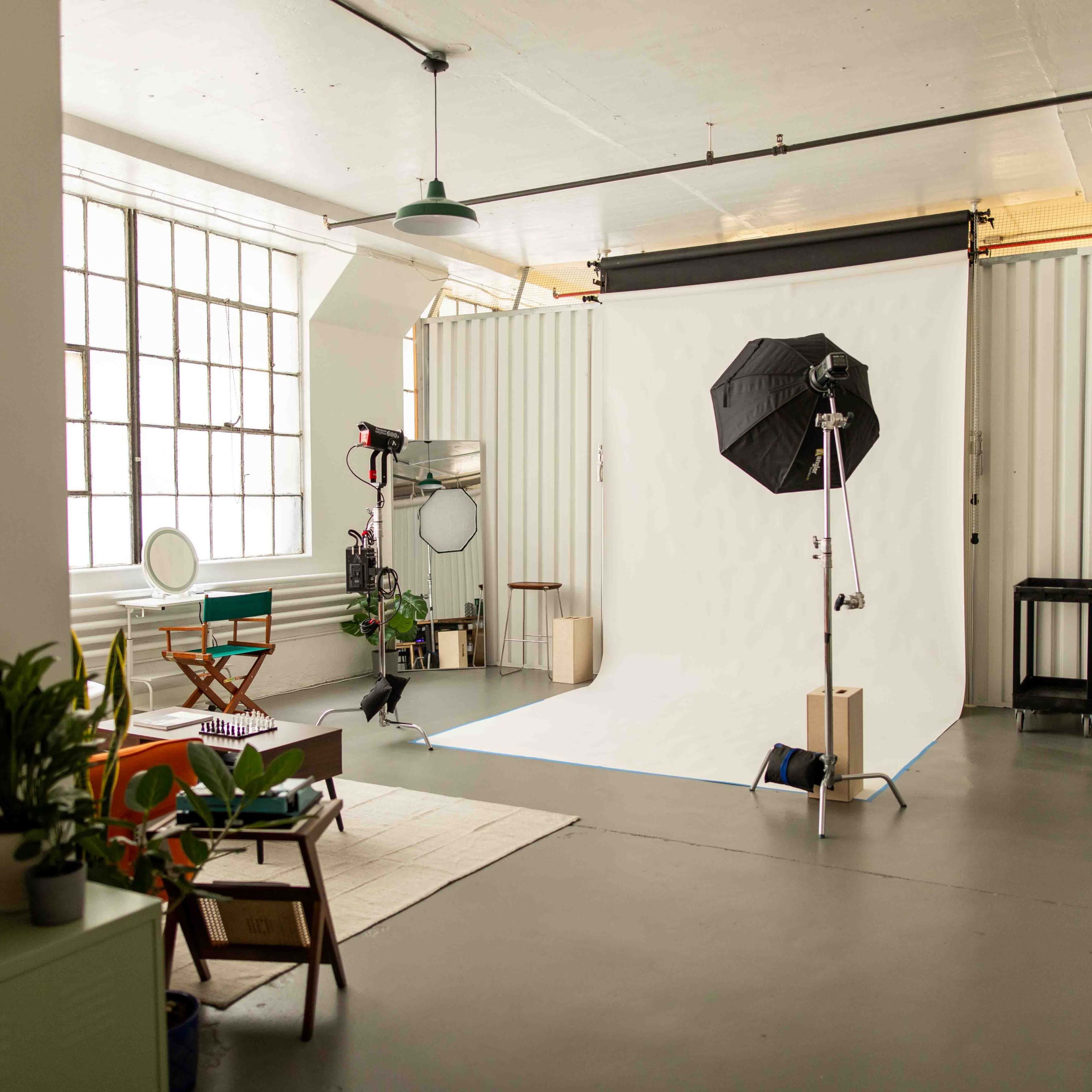 A well-lit photography studio with a seamless white backdrop, lighting equipment, and a few pieces of furniture.