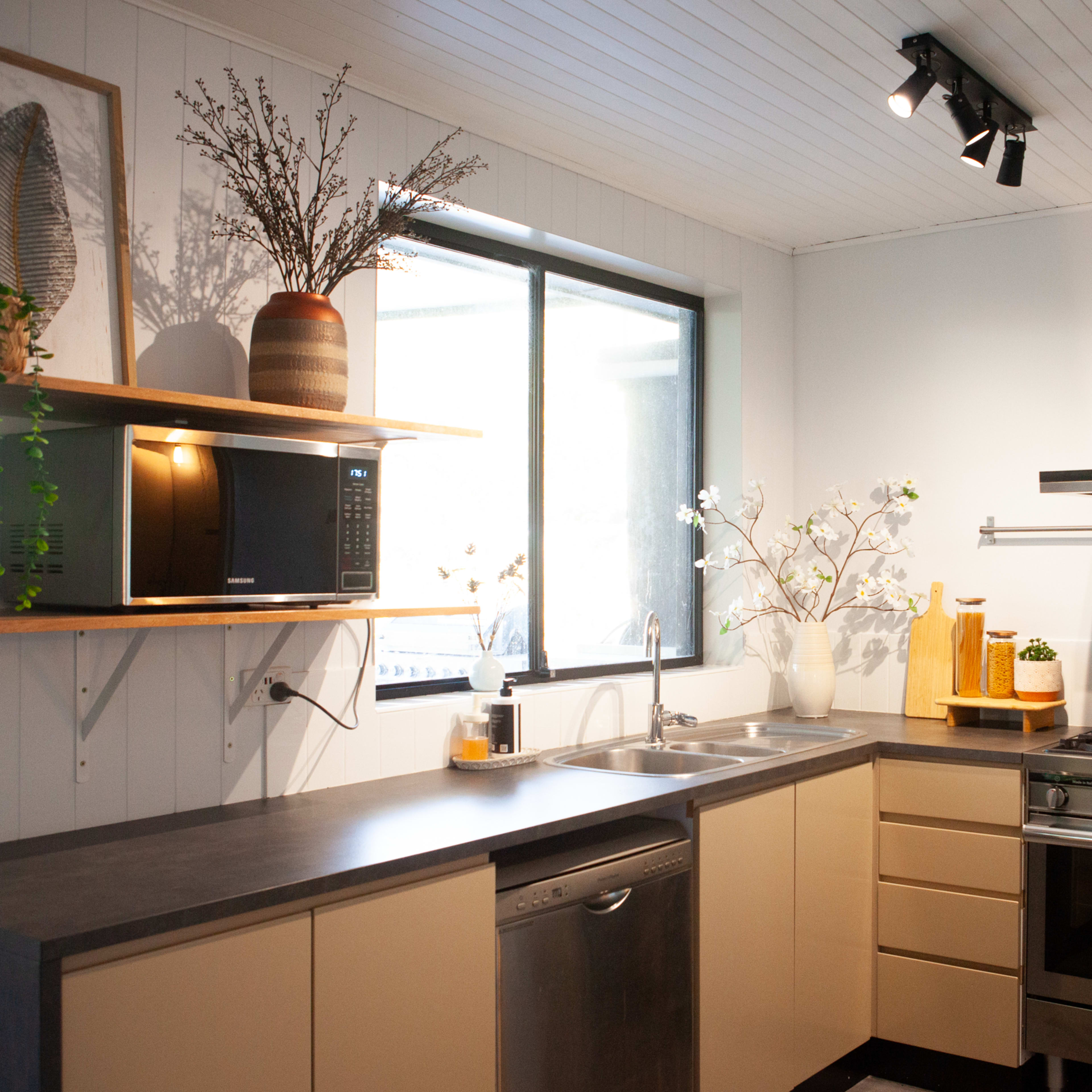 A modern kitchen features a stainless steel stove, an organized countertop, a sink, and shelves with decorative plants and kitchen appliances.