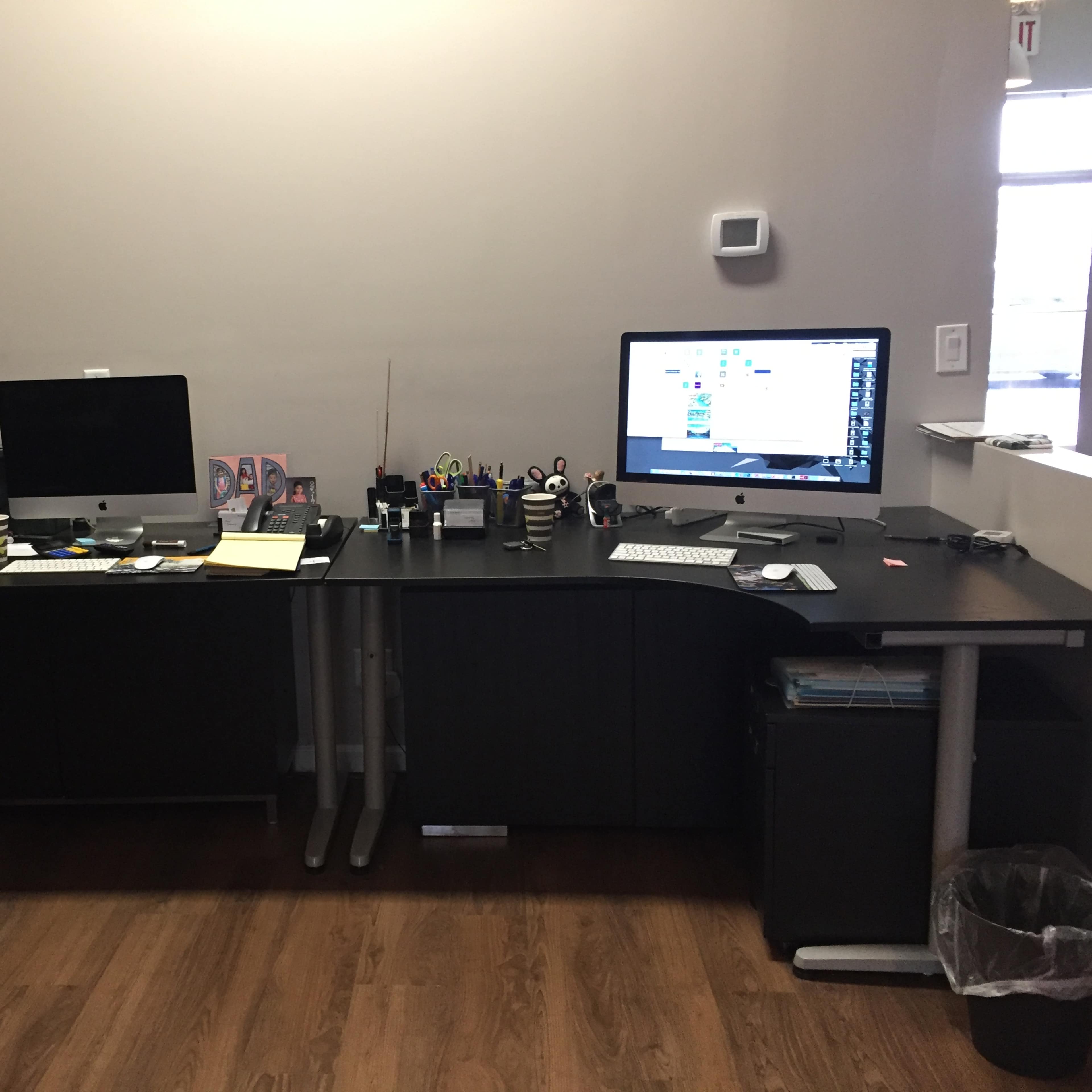 A dual workstation setup features two computers, a printer, and various office supplies on a dark wood desk.