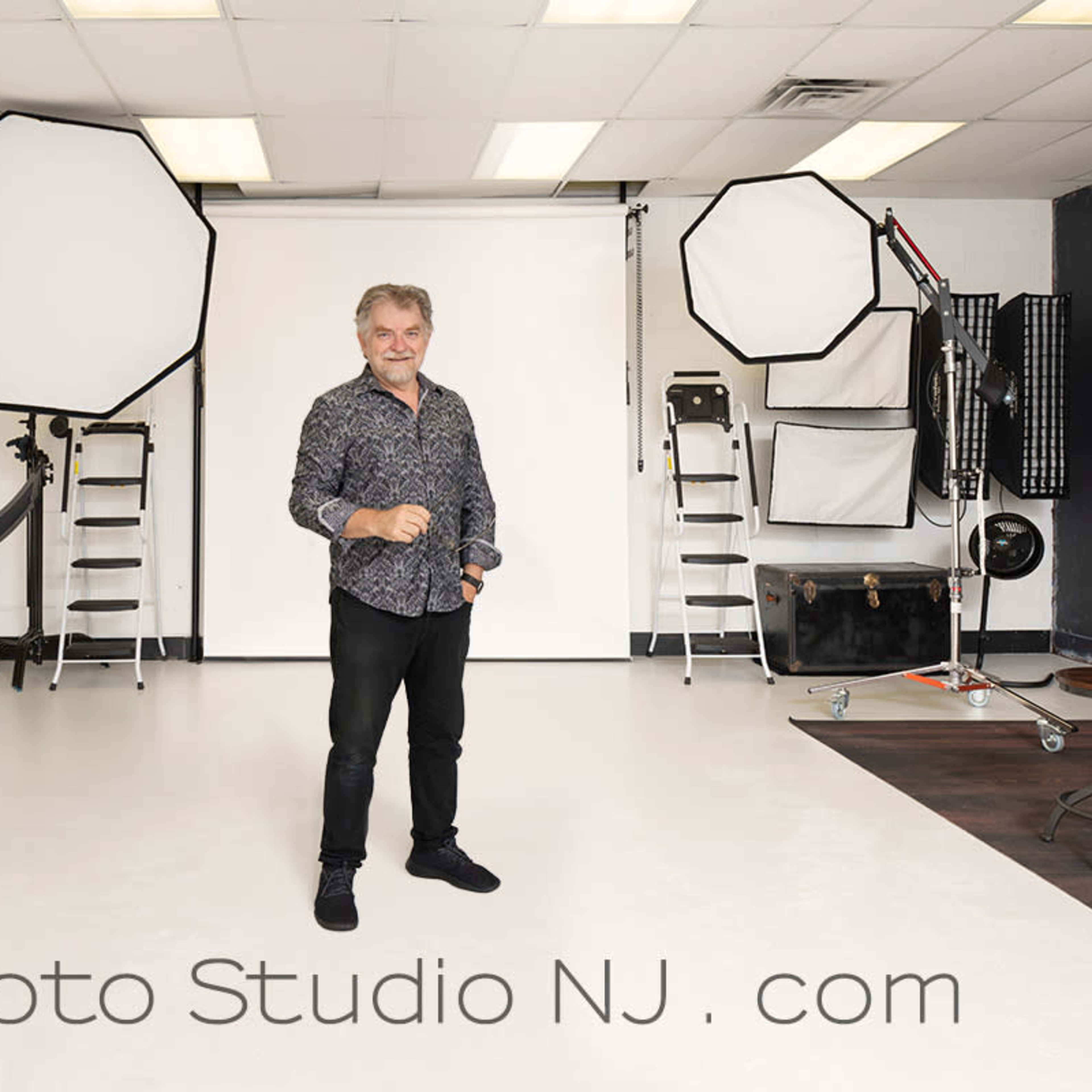 A man stands in a well-equipped photography studio with various lighting setups and backdrops.