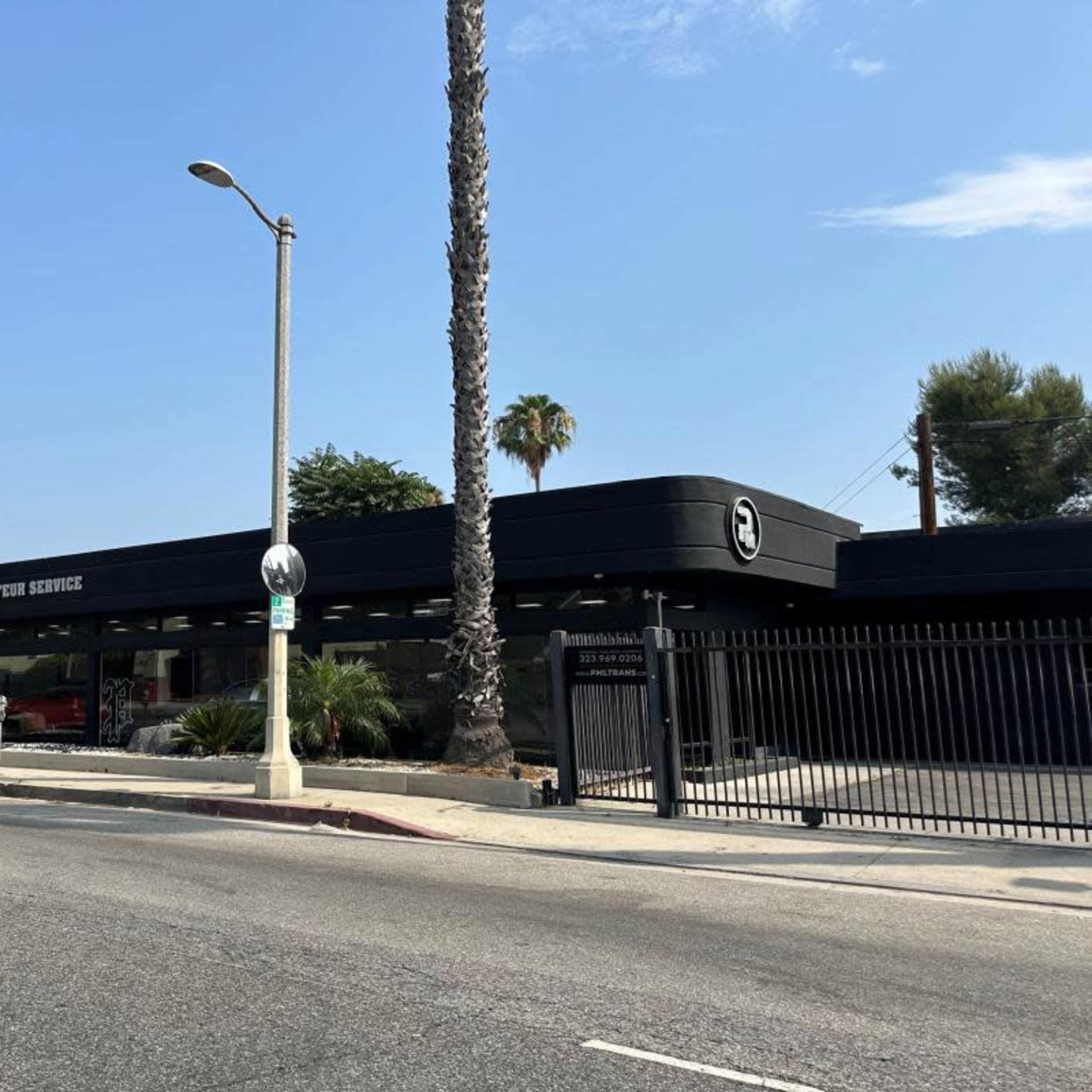 A modern building with large windows and a sign that reads "P.H.S. Rehabilitation Services," flanked by tall palm trees along a road.