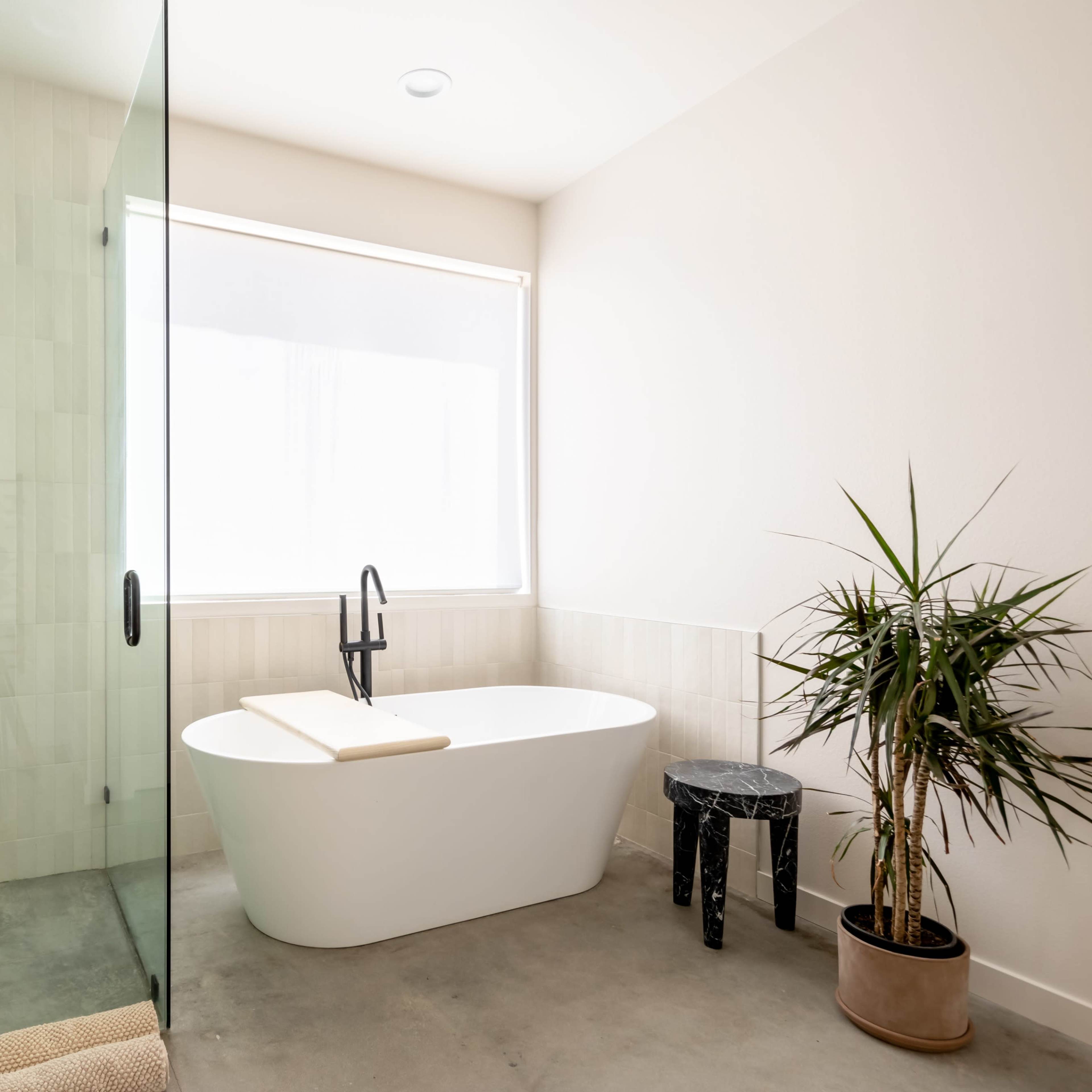 A modern bathroom featuring a freestanding bathtub, a glass shower enclosure, and a potted plant in the corner.