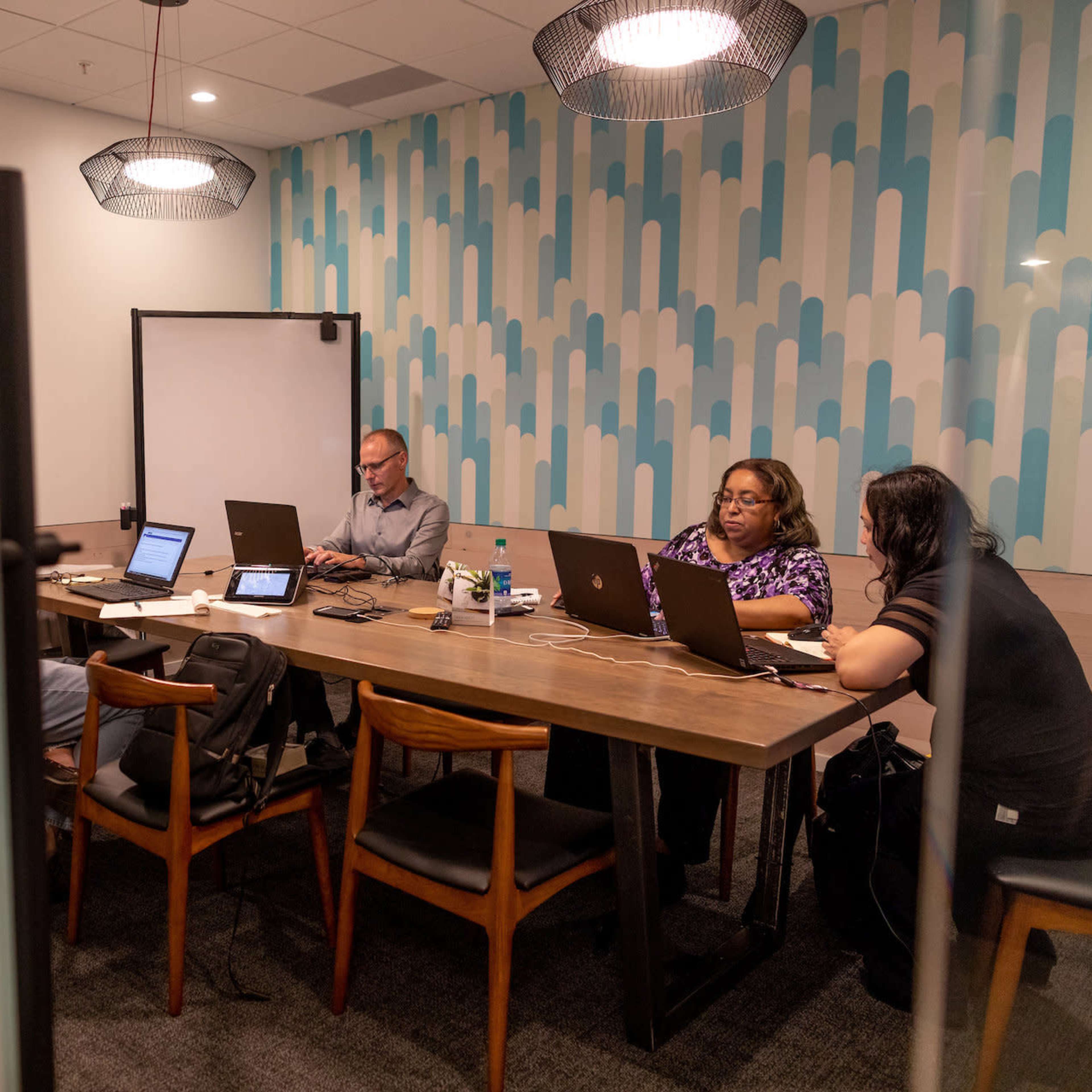 A group of four professionals collaborates at a conference table in a well-lit meeting room, with laptops and tablets in use.
