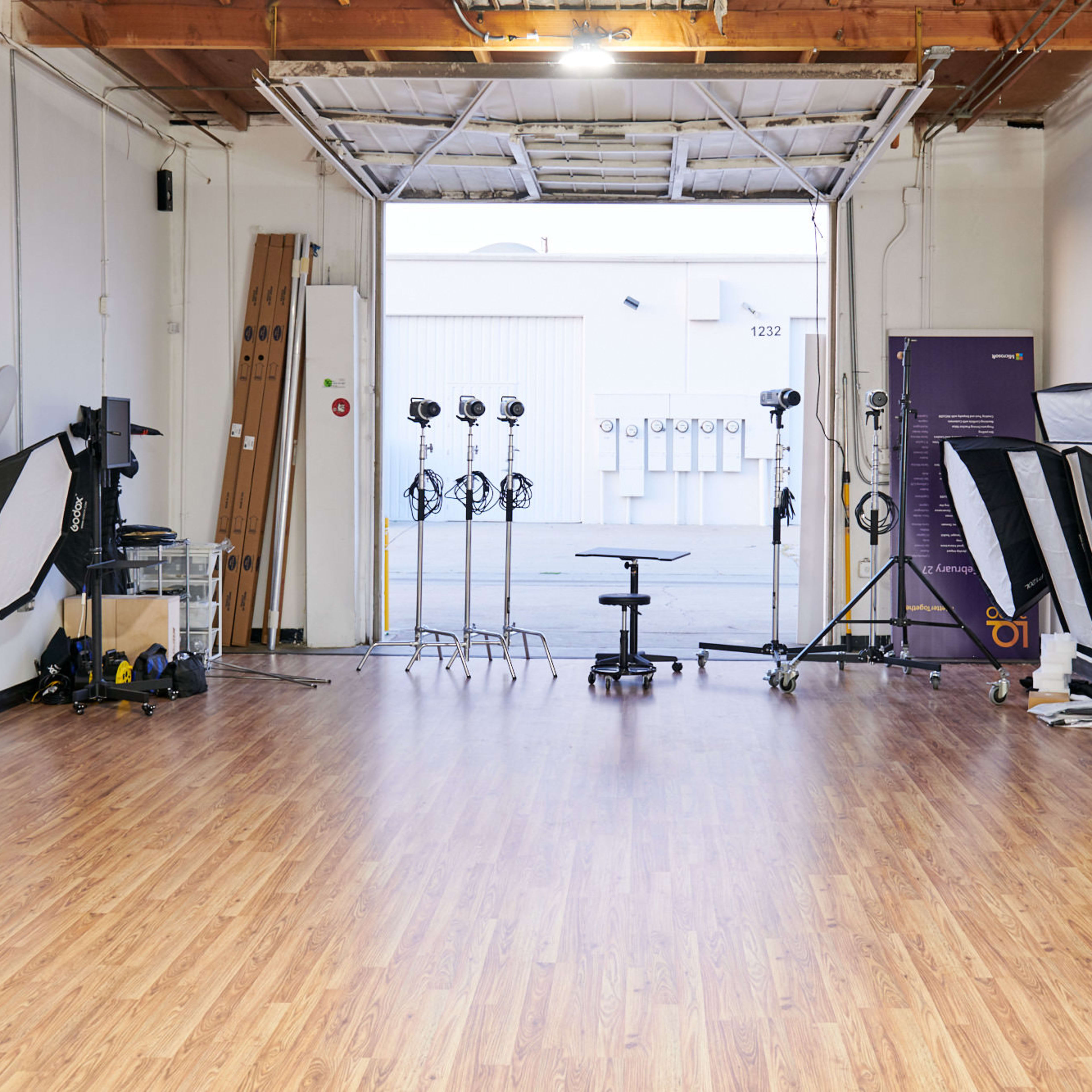 A spacious photography studio with wooden flooring, multiple light stands, softboxes, and a central rolling chair, all set up for a shoot.