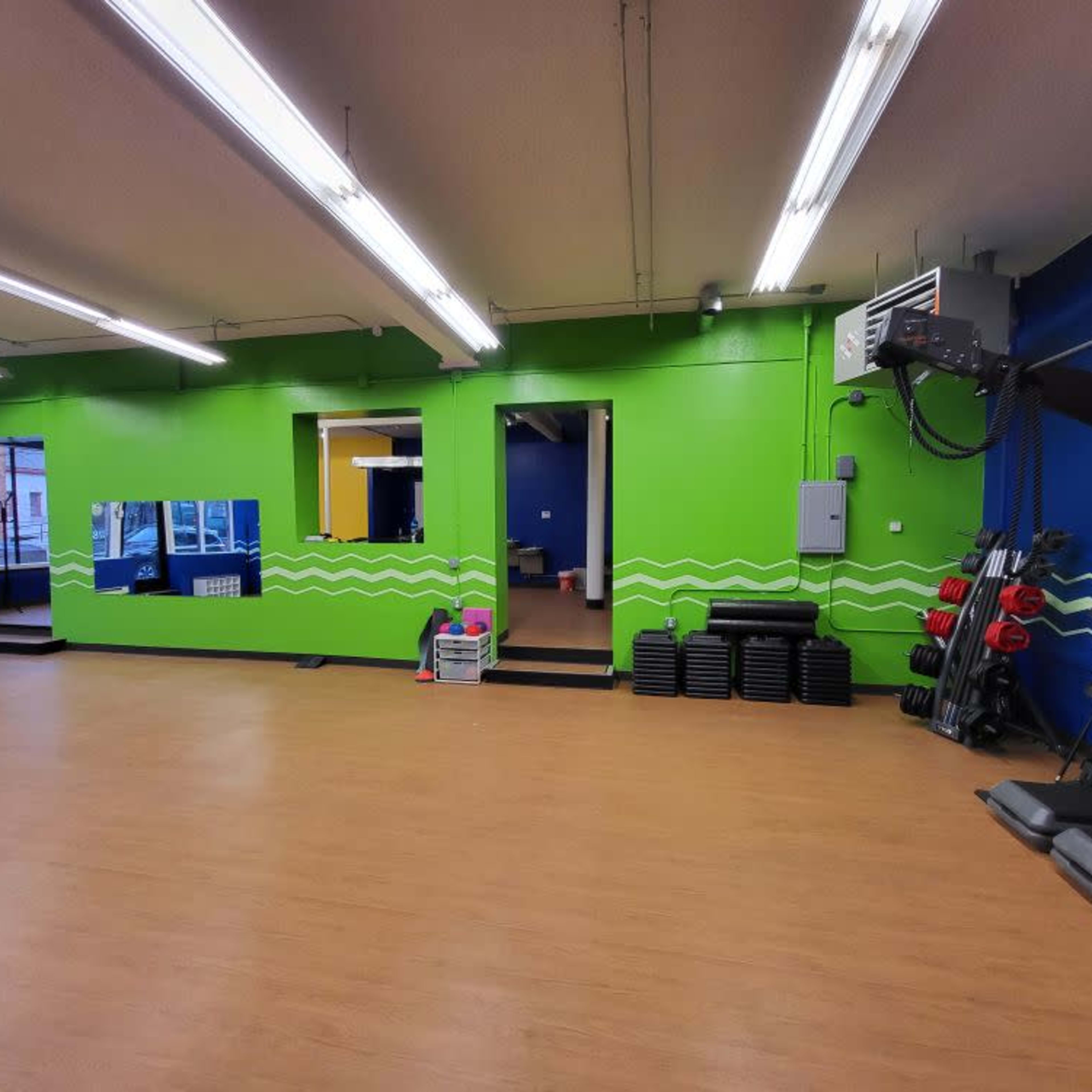 An exercise studio with a brightly colored green and blue interior, featuring fitness equipment stacked along one wall.