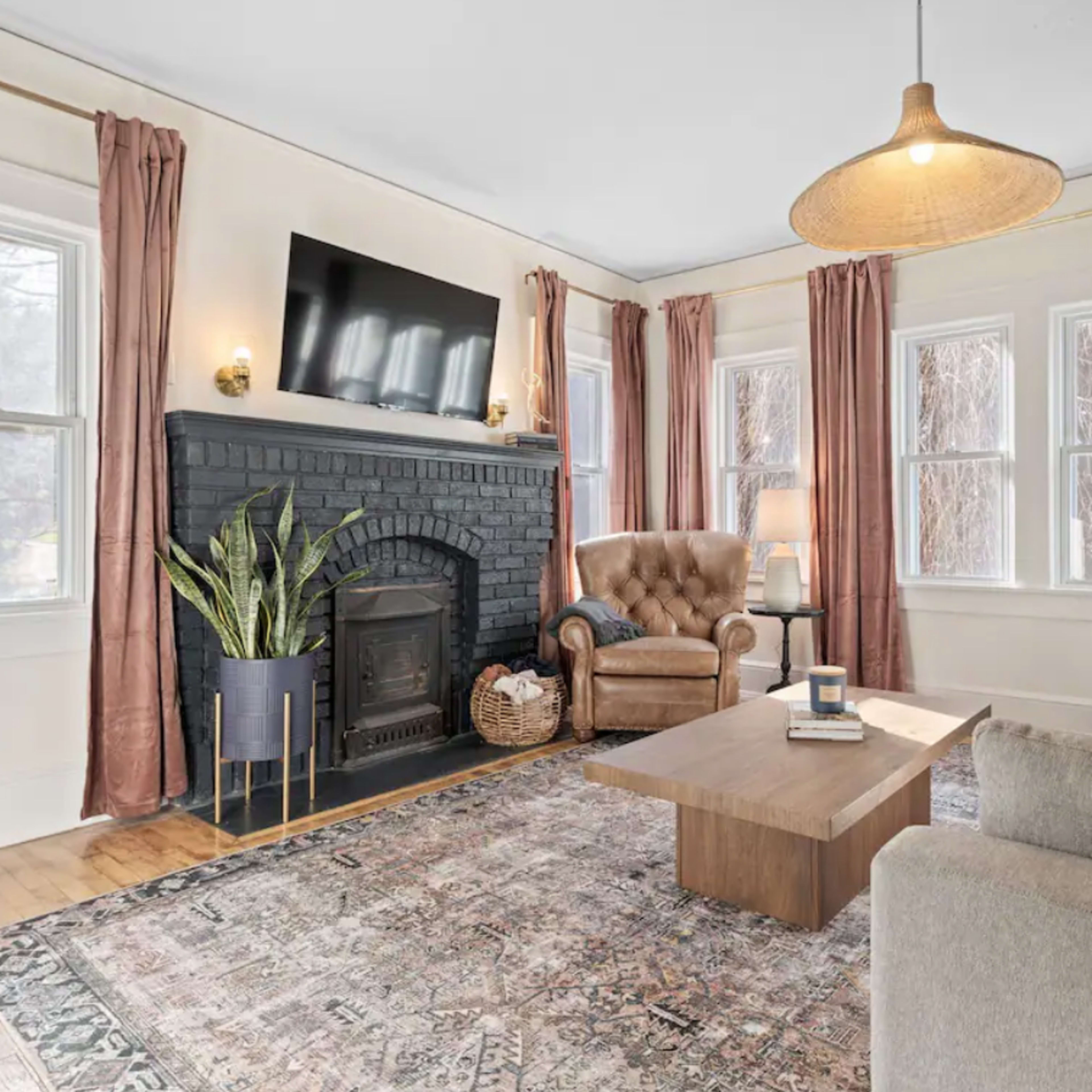 The living room features a dark-brick fireplace, a large window, a sofa, an armchair, and a coffee table.